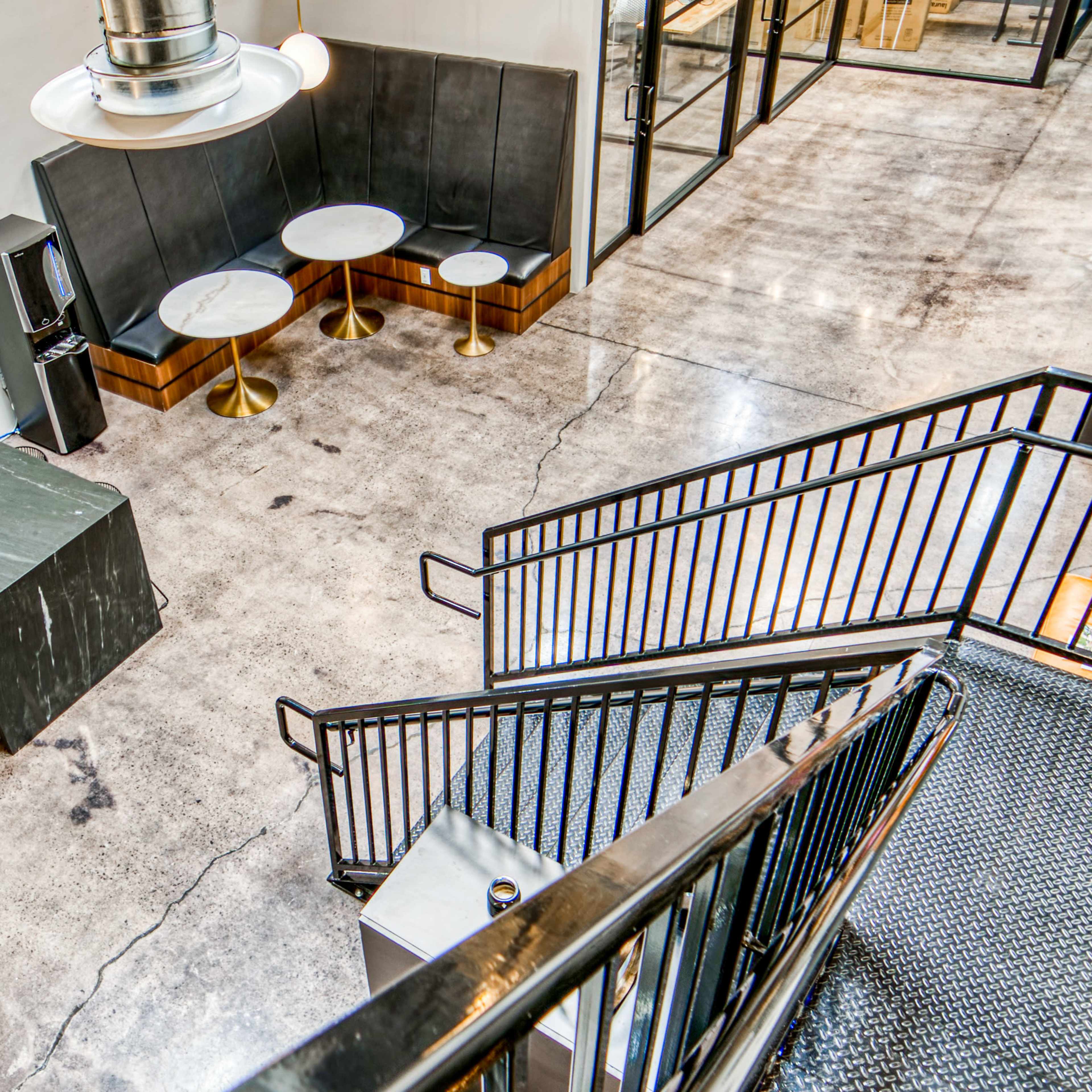 A modern kitchen area with a marble countertop, metal fixtures, and a staircase leading to an upper level, all set in a spacious, industrial-style interior.