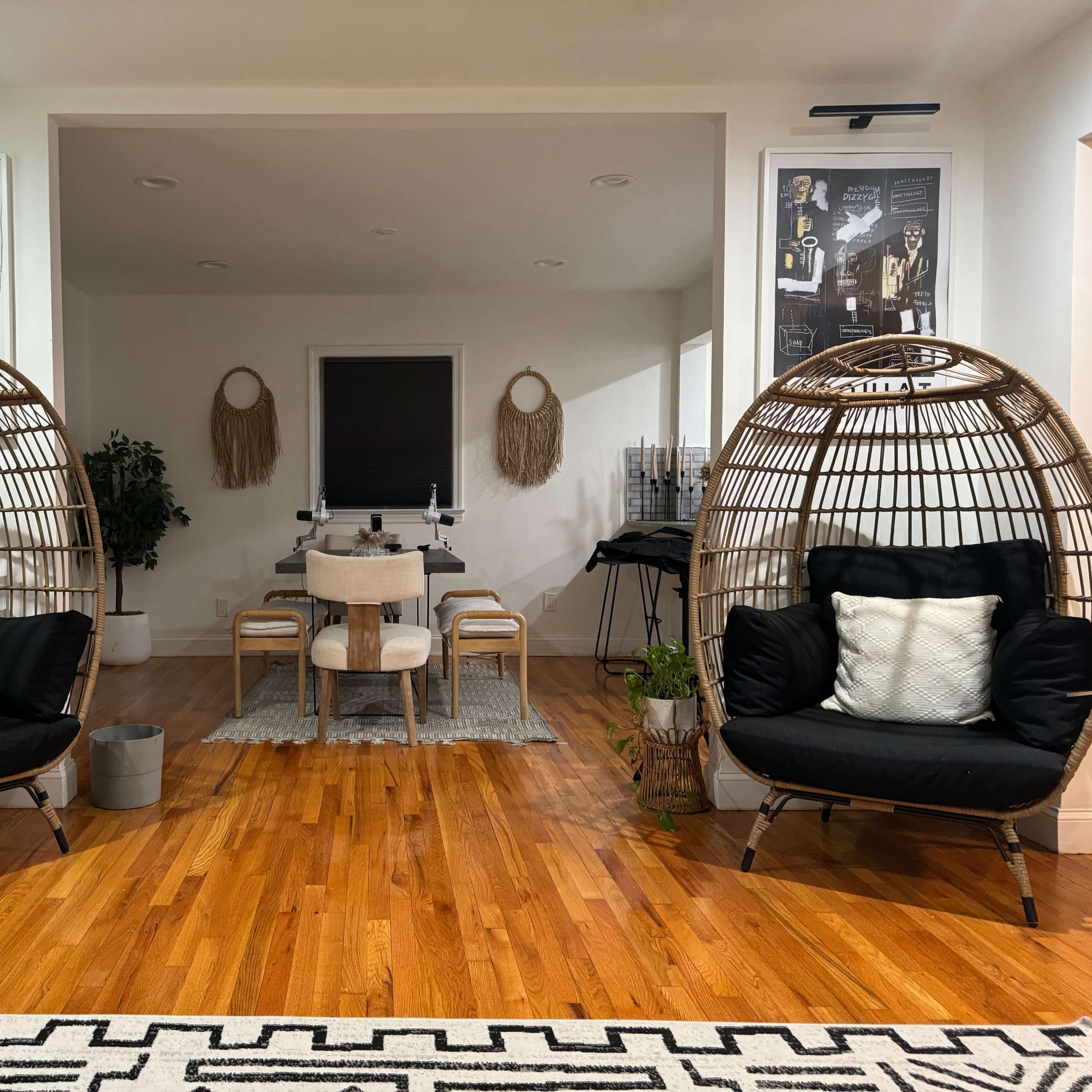 A modern living space featuring two large, rounded wicker chairs on either side, with a dining area and decorative elements in the background.