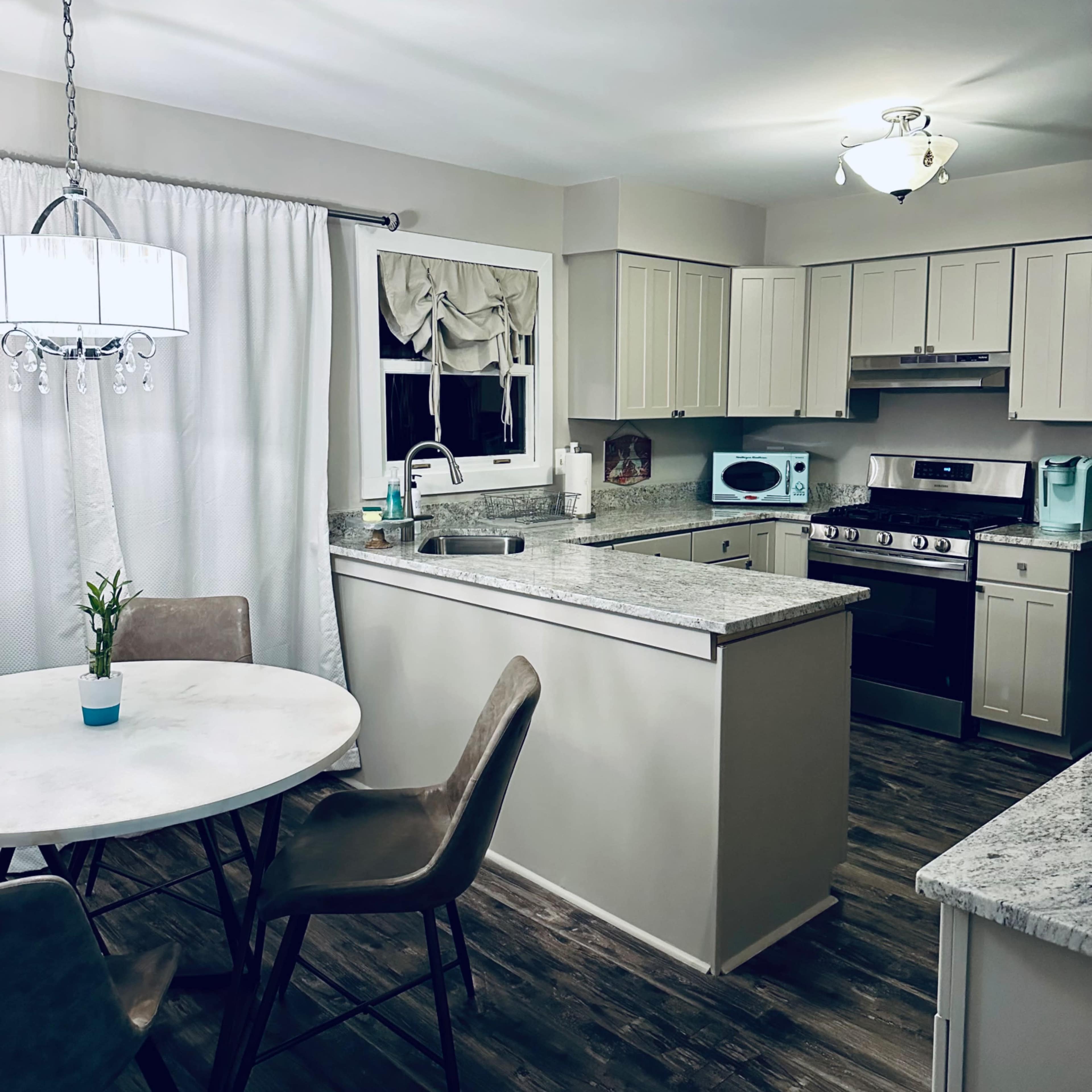 A modern kitchen features light-colored cabinets, a round dining table, and stainless steel appliances.