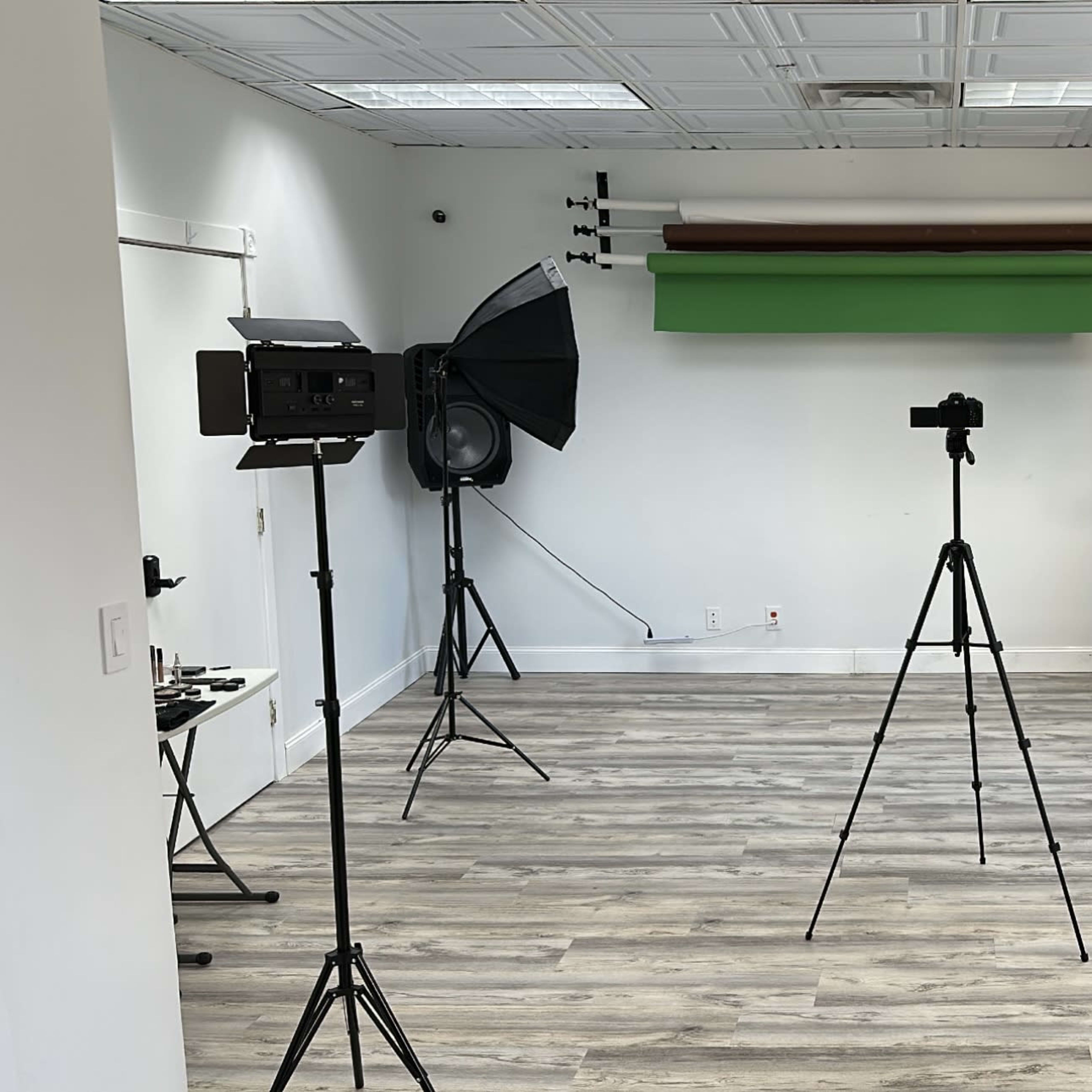 A photography studio featuring three tripods with cameras, two softbox lights, and a green backdrop.