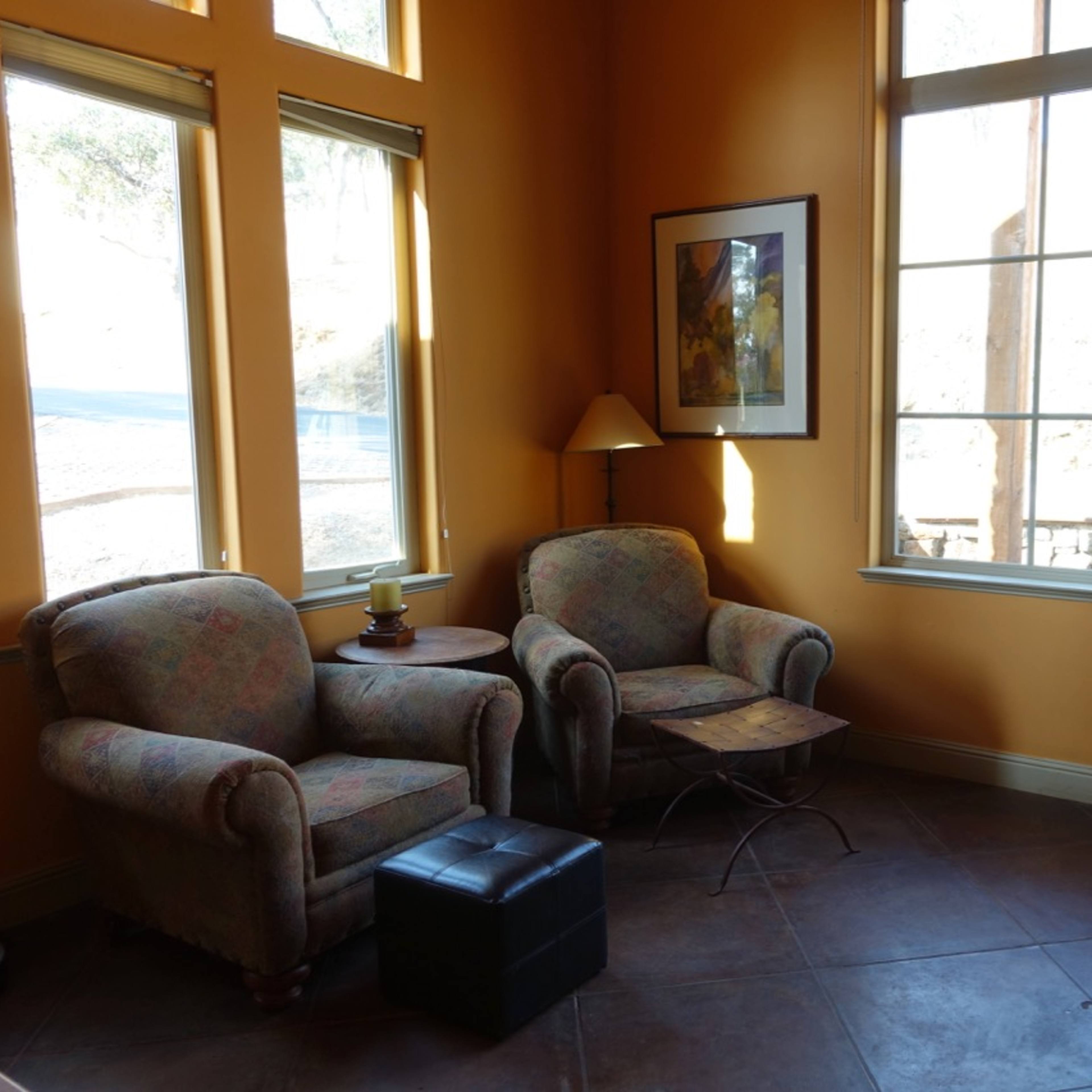 A cozy corner of a room with two upholstered chairs, a small table between them, and a nearby window allowing natural light to enter.