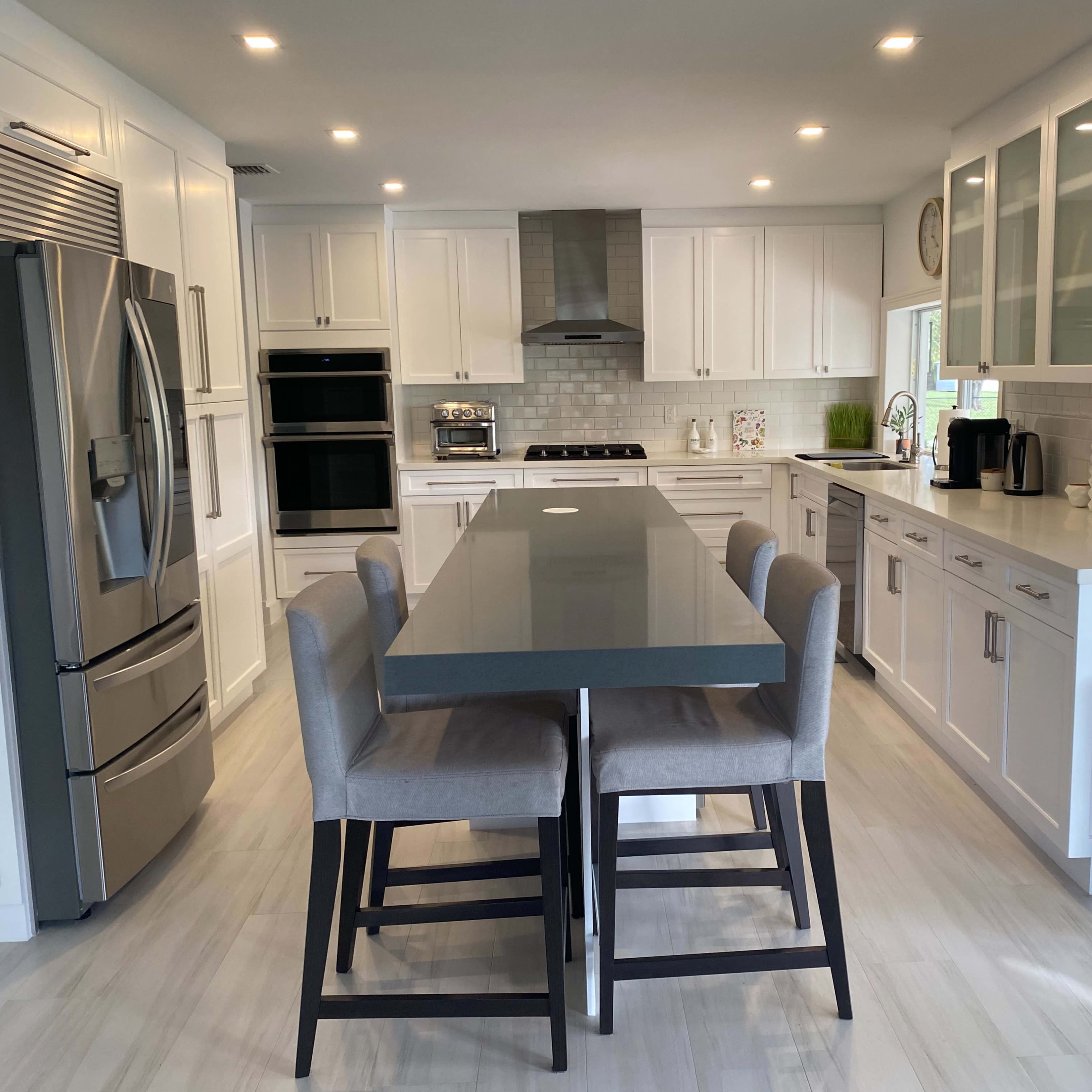 A modern kitchen featuring white cabinetry, stainless steel appliances, and a long island with seating for four.