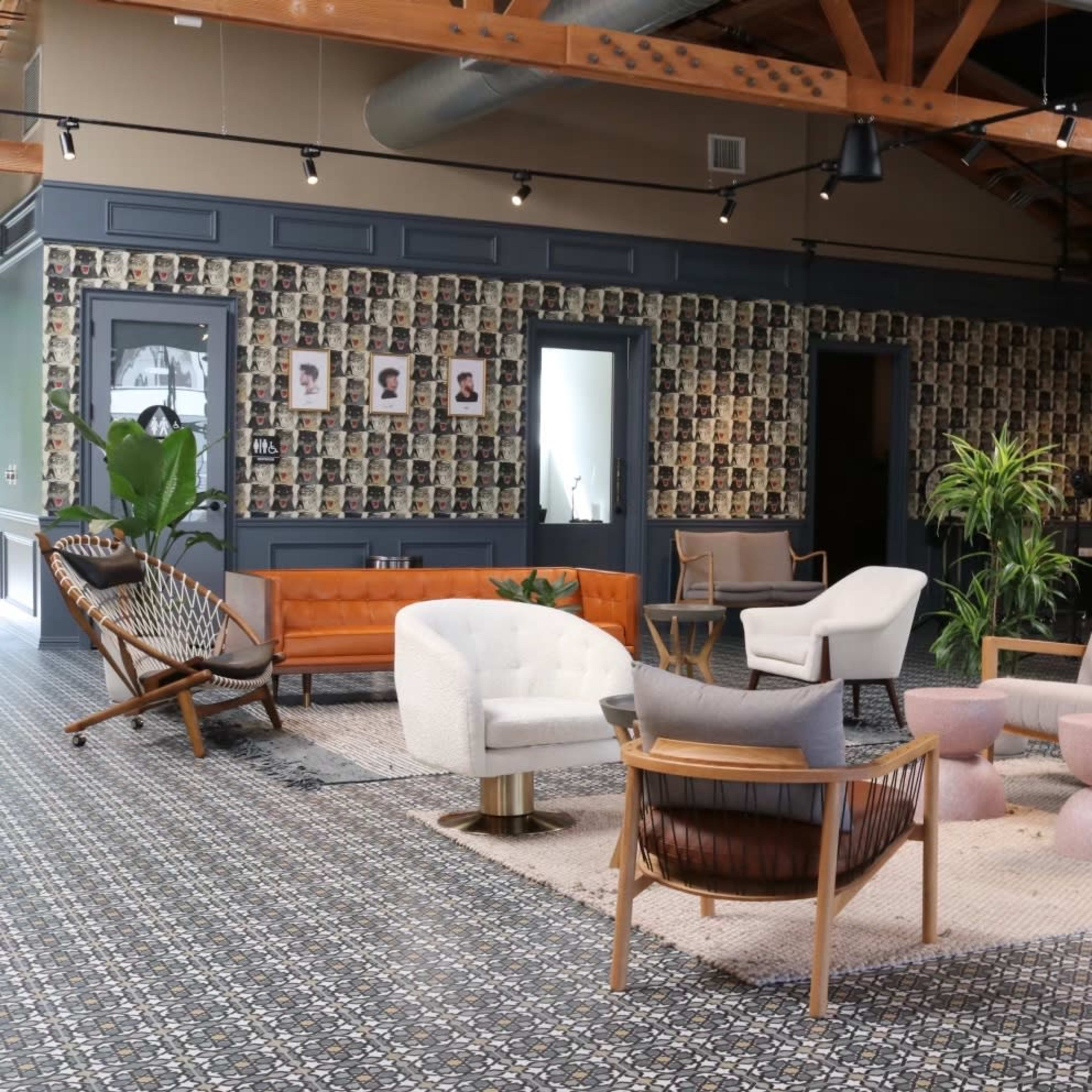 A modern interior space features various seating options arranged around a light-colored area rug, with a wall adorned by numerous framed photographs.