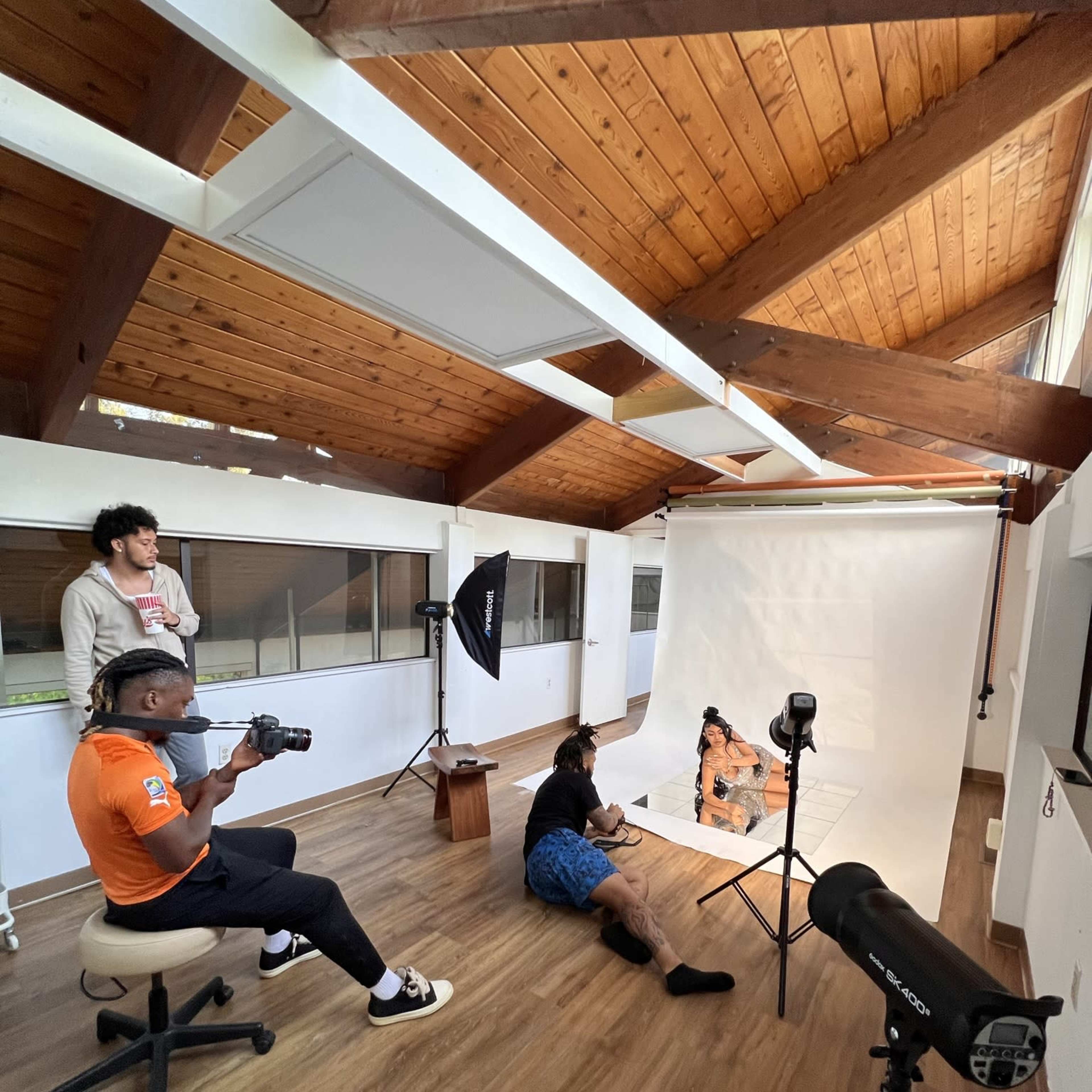 A group of people are participating in a photo shoot inside a well-lit studio with wooden ceilings and a blank backdrop.