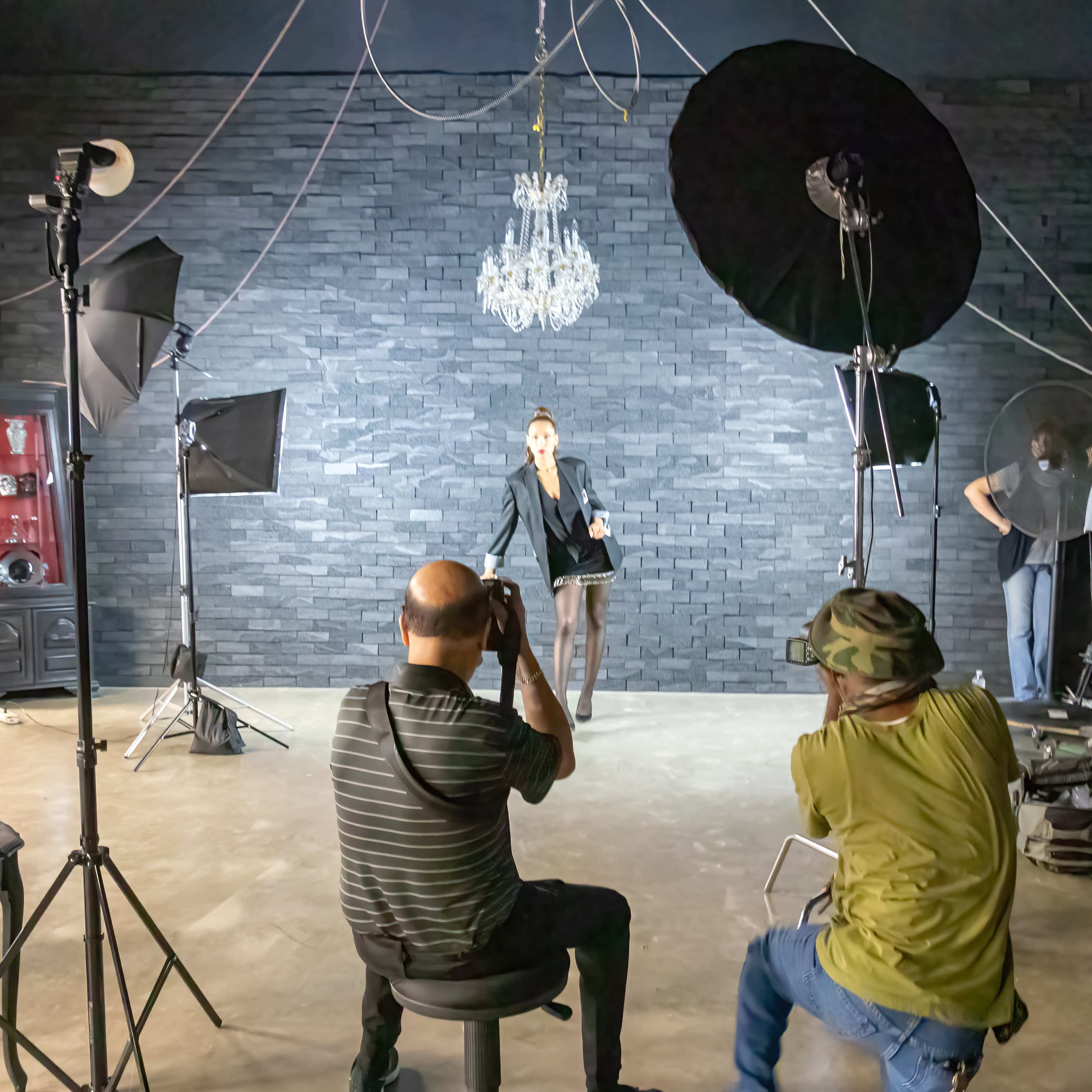 A model poses for a photoshoot in a studio surrounded by multiple photographers and lighting equipment.
