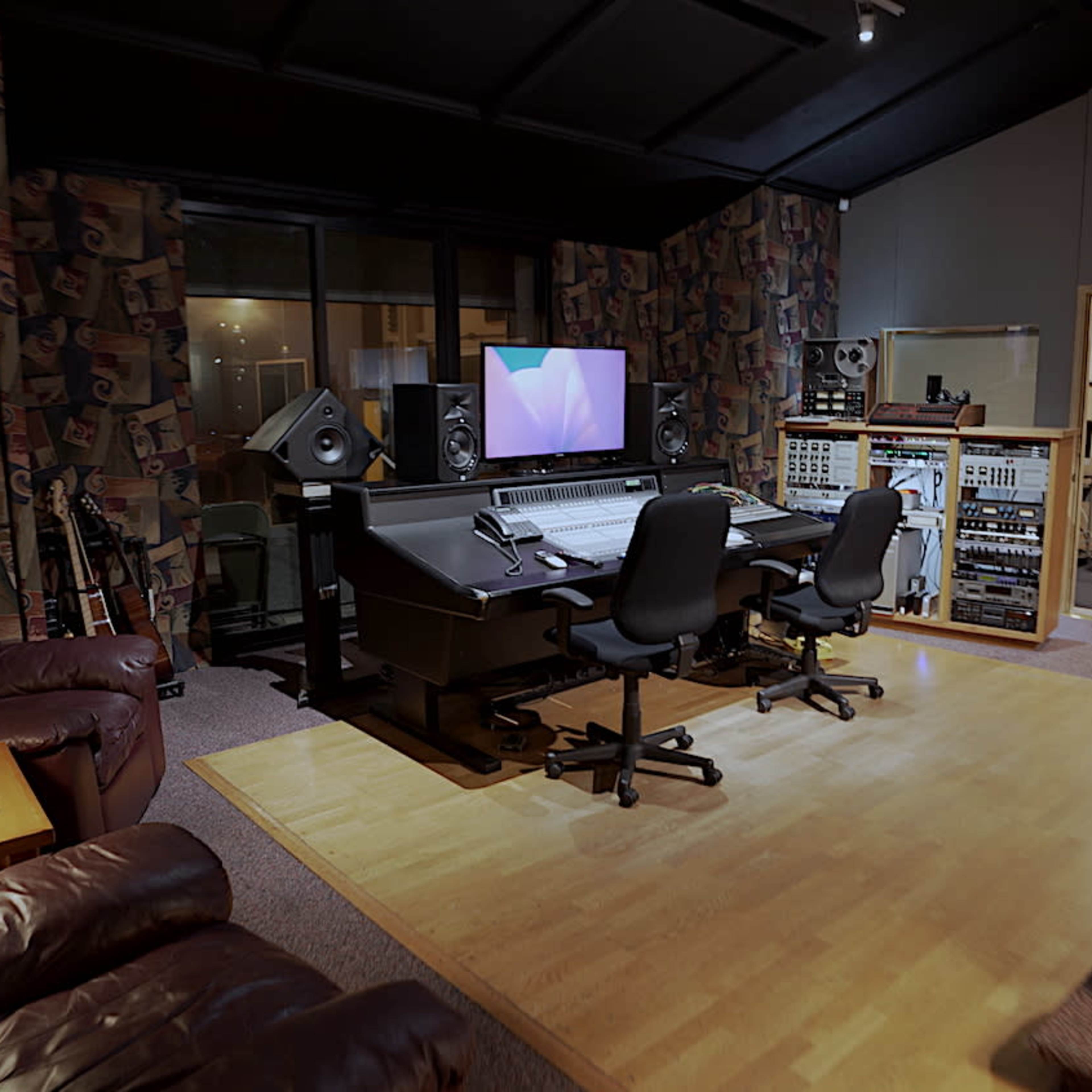 A well-equipped music recording studio featuring a mixing desk, monitors, and comfortable seating areas.