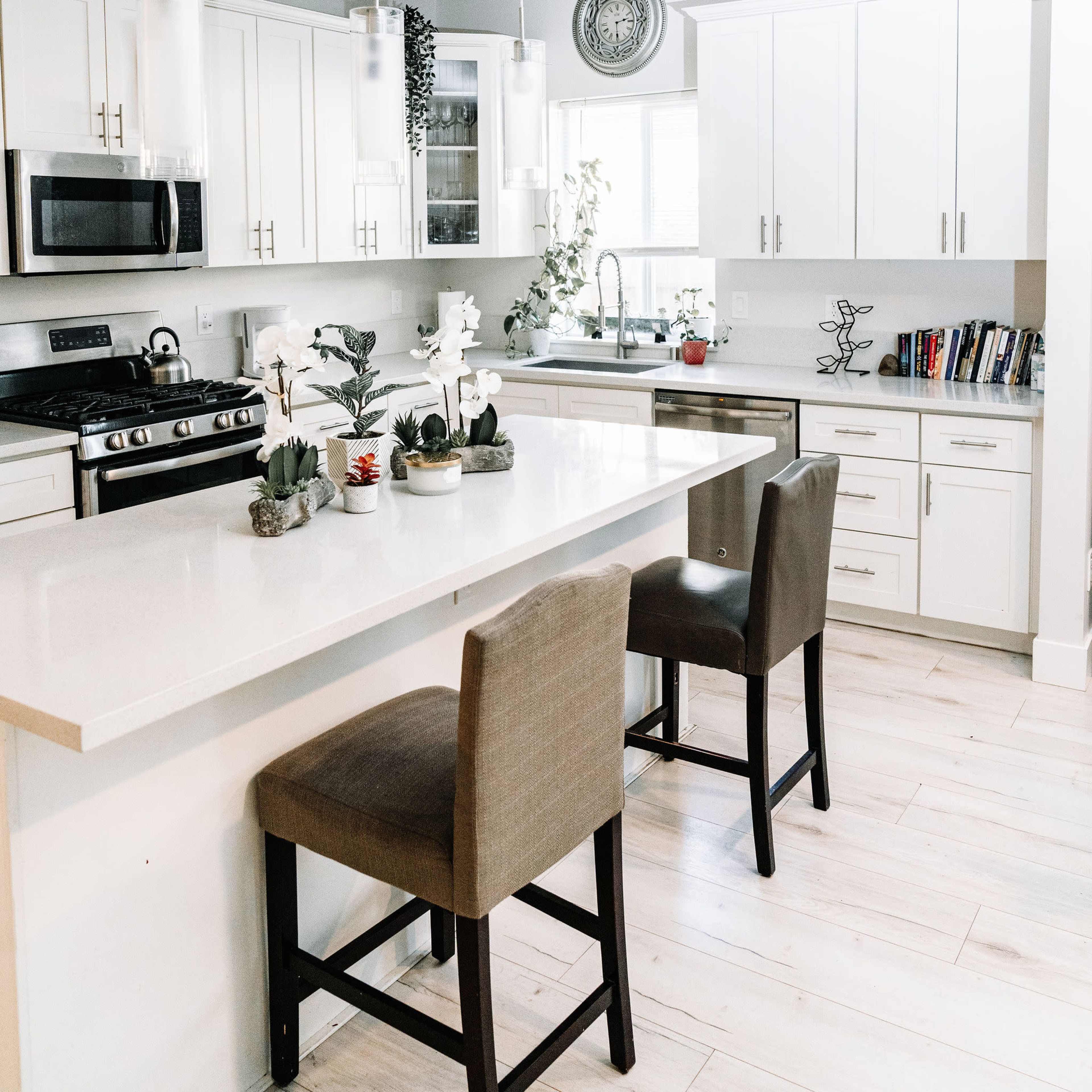 A modern kitchen features white cabinets, a large island with two brown bar stools, and pendant lighting above.