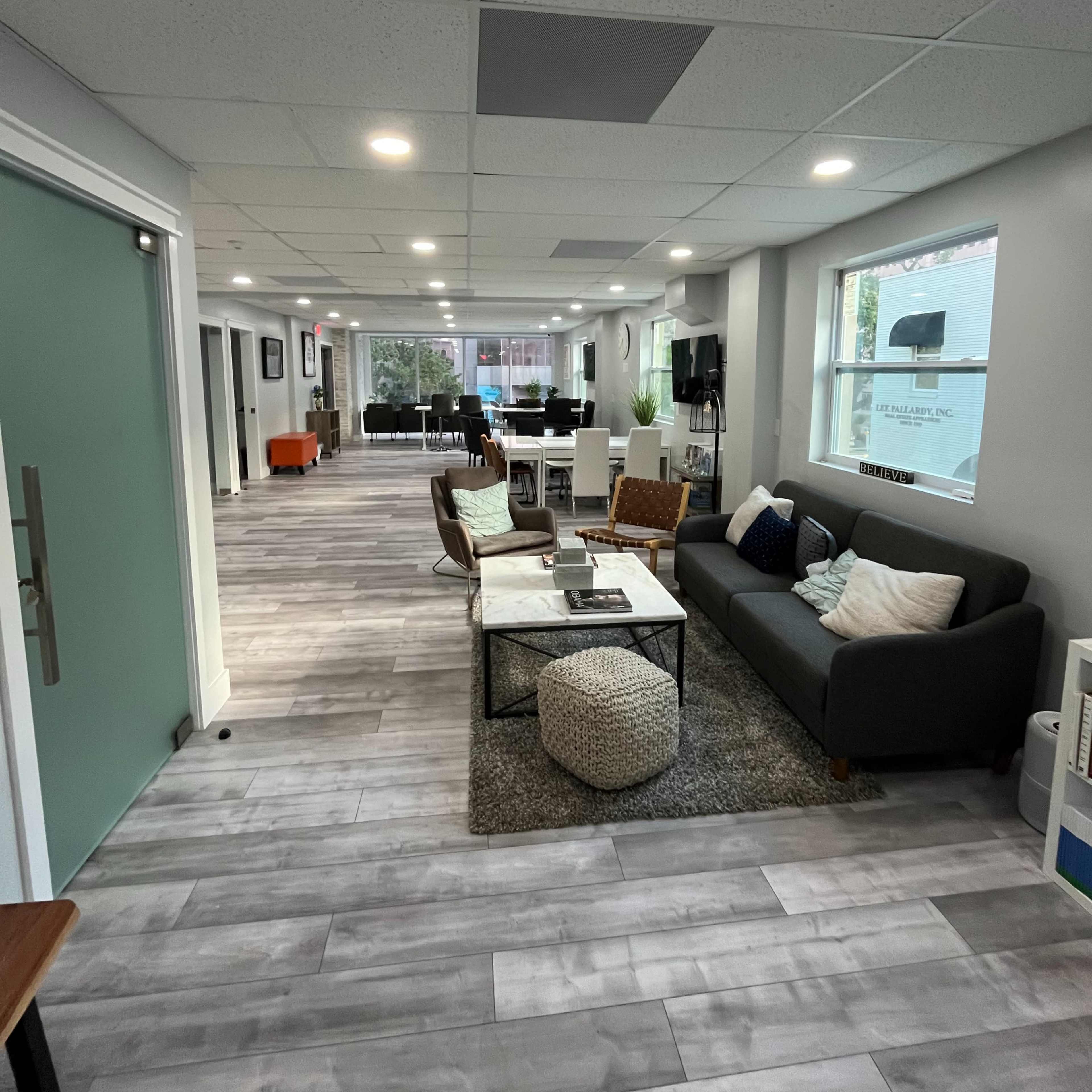 A modern office interior with a seating area, a light gray tile floor, and large windows along one side.