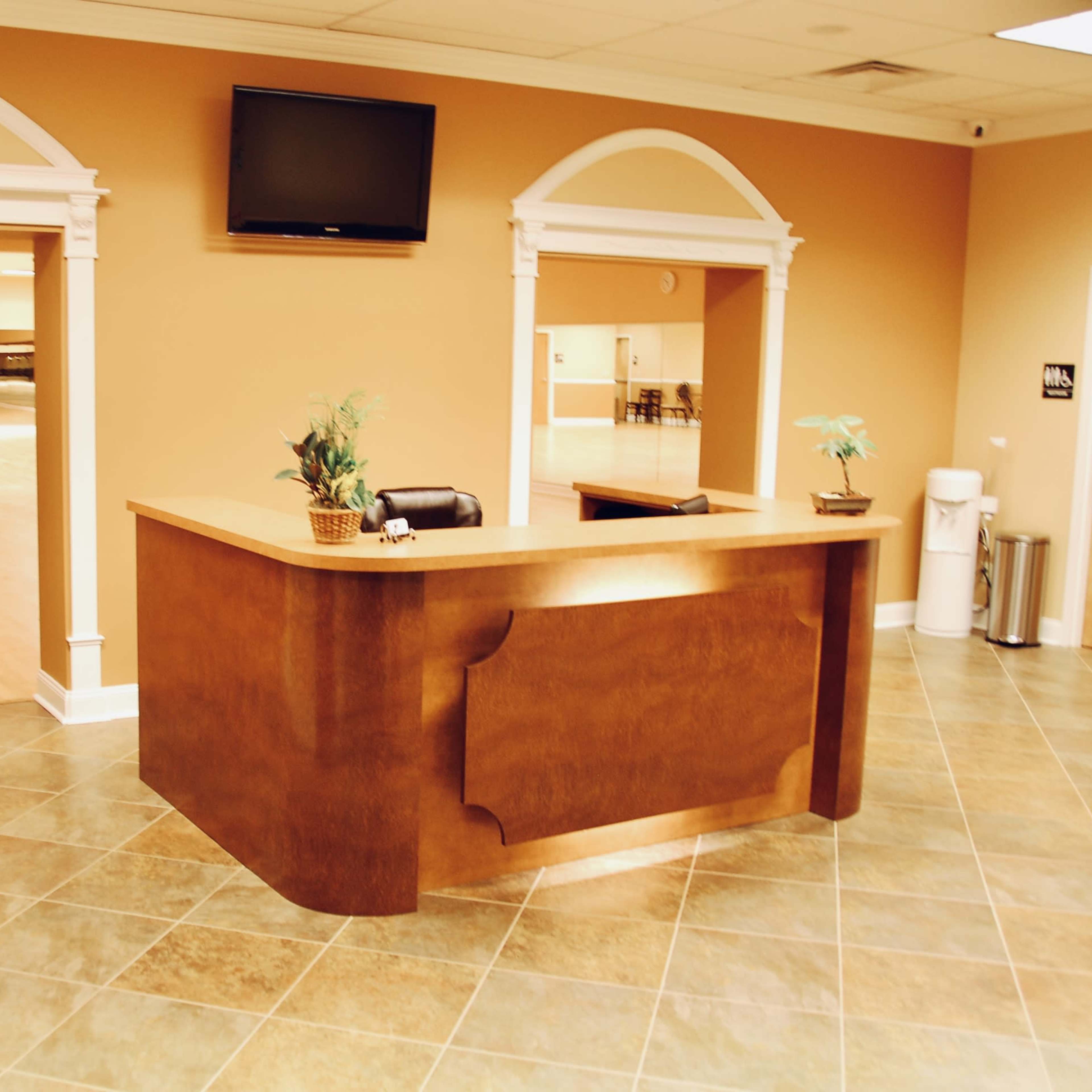 A reception area with a wooden desk, two archways leading to a large open space, and a television mounted on the wall.