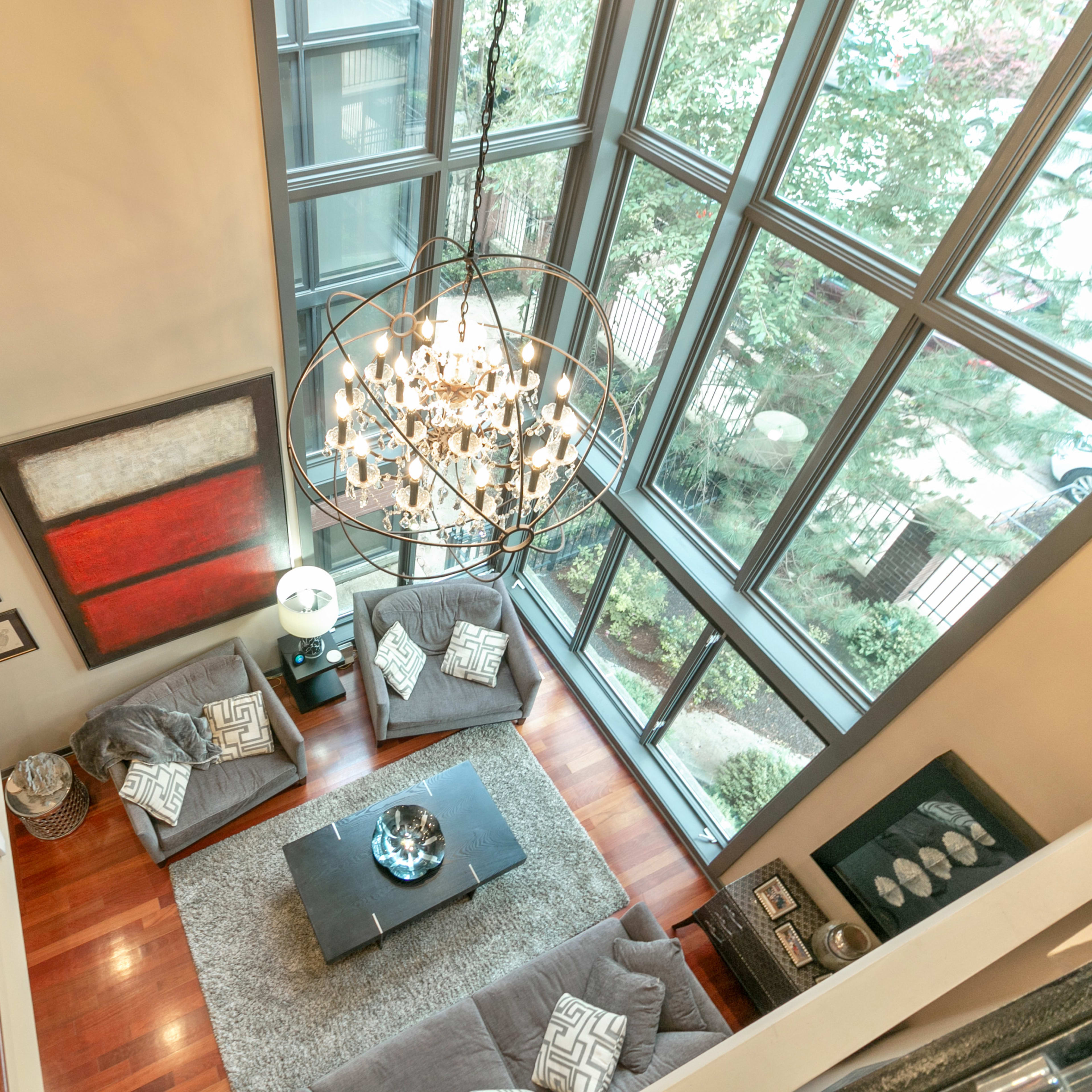 A spacious living room with large windows, a modern chandelier, and a staircase leading to an upper level.