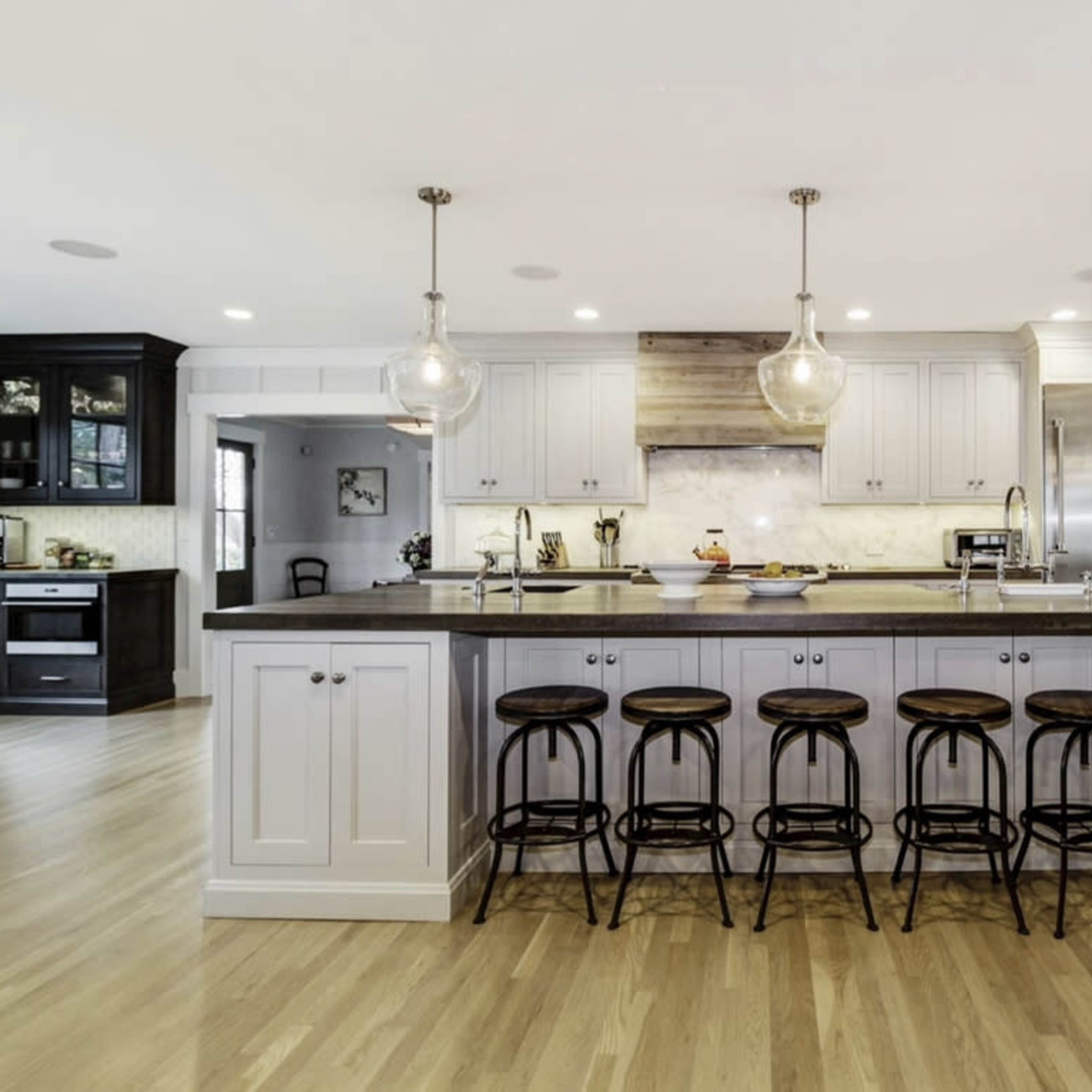 A modern kitchen featuring a central island with six bar stools, pendant lighting, and stainless steel appliances.