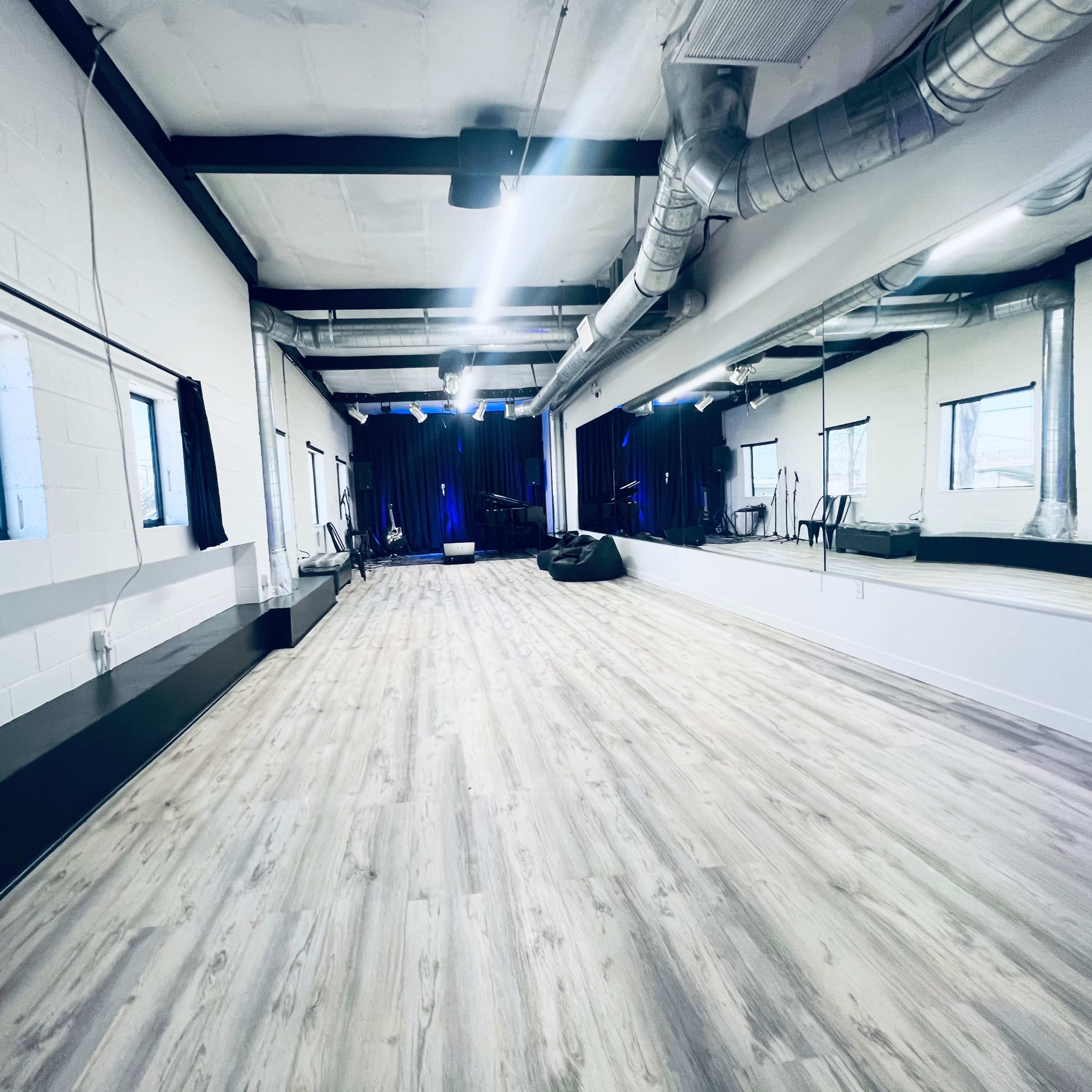 A spacious, well-lit room with wooden flooring, large mirrors, and black curtains at the windows.