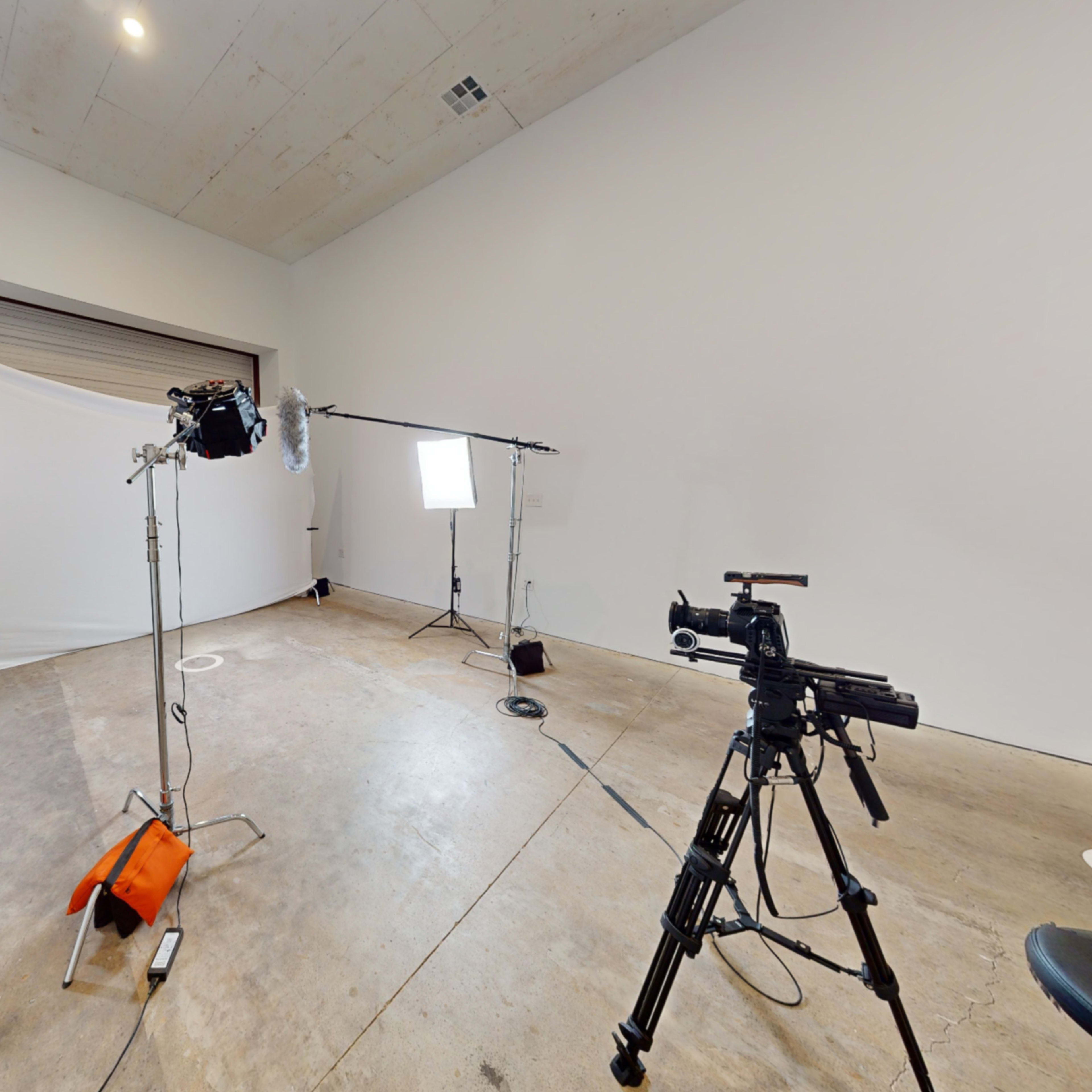 A sparse studio with various lighting equipment and cameras set up on a concrete floor.