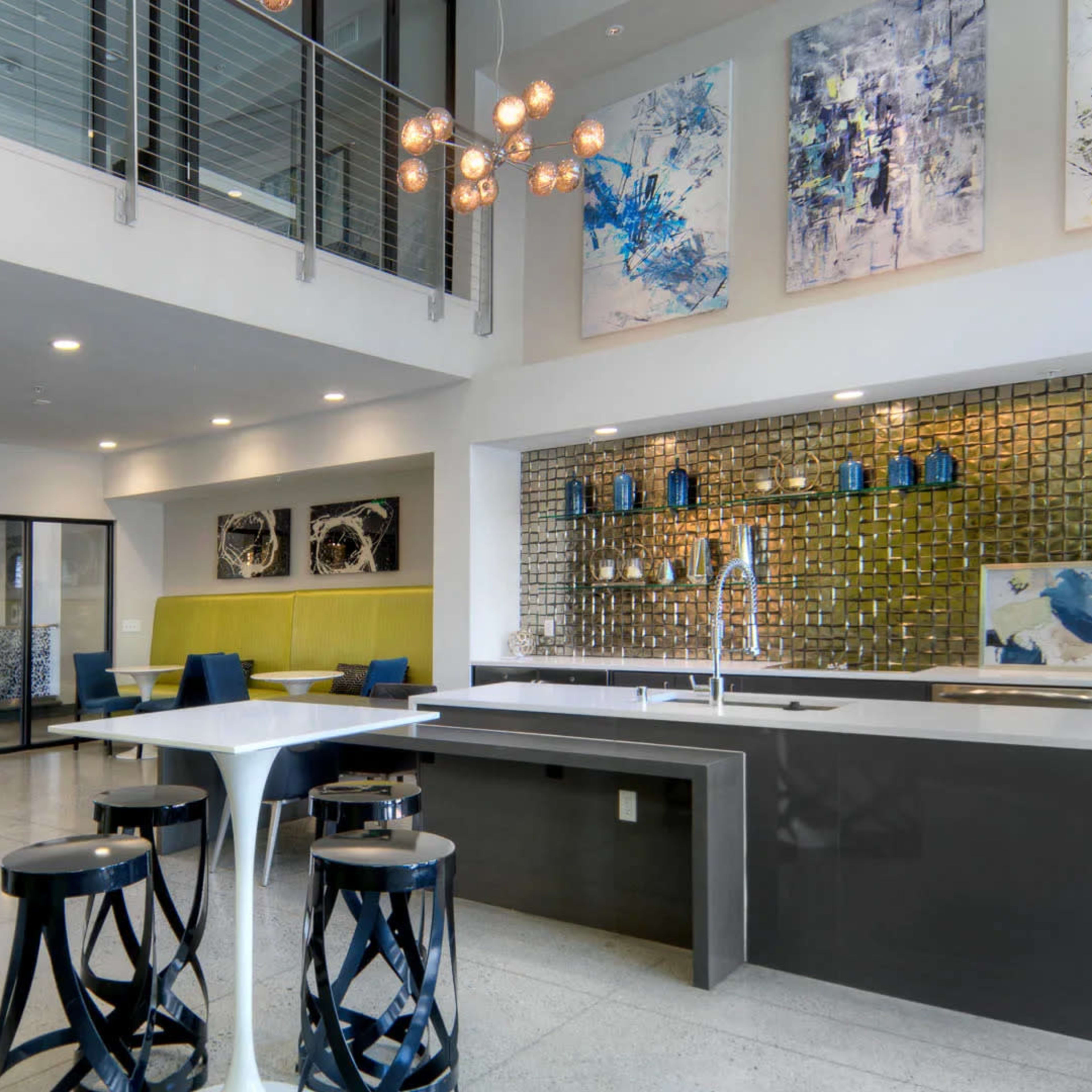 A modern lobby area with a kitchen island, seating areas, and abstract art on the walls, featuring a mix of textures and colors.