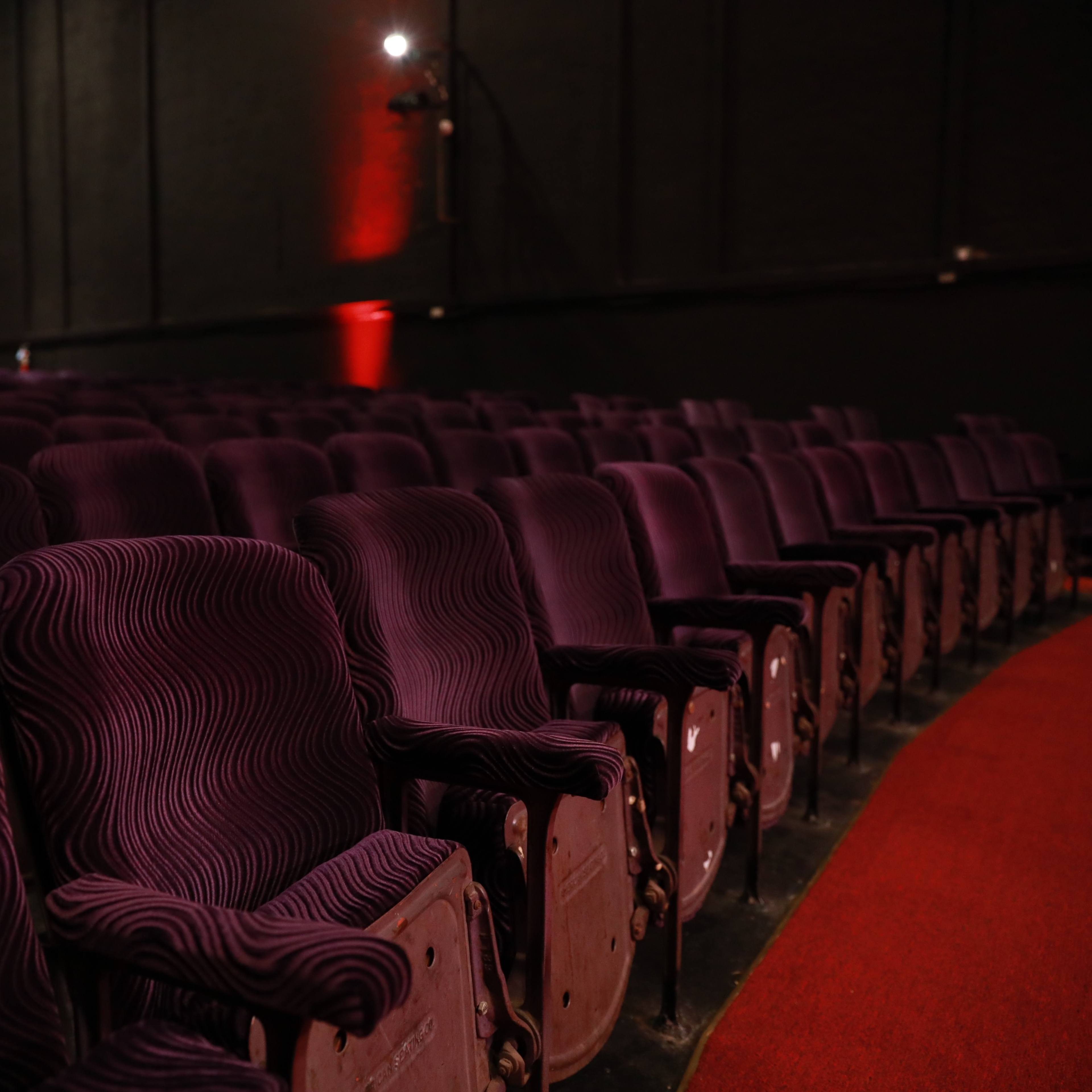 A row of empty purple theater seats in a dimly lit auditorium.