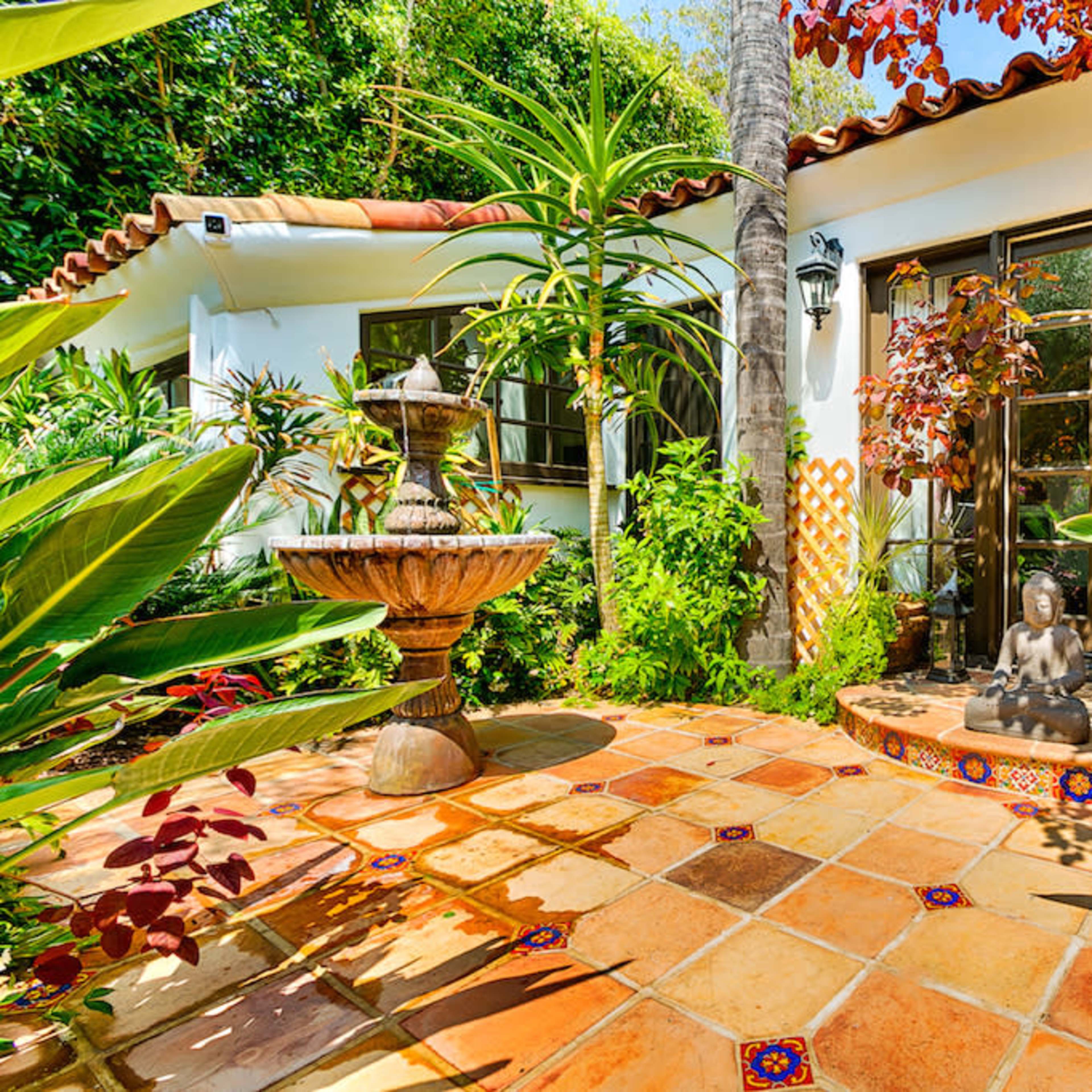 A vibrant courtyard with a central fountain, surrounded by lush greenery and terracotta tiles.