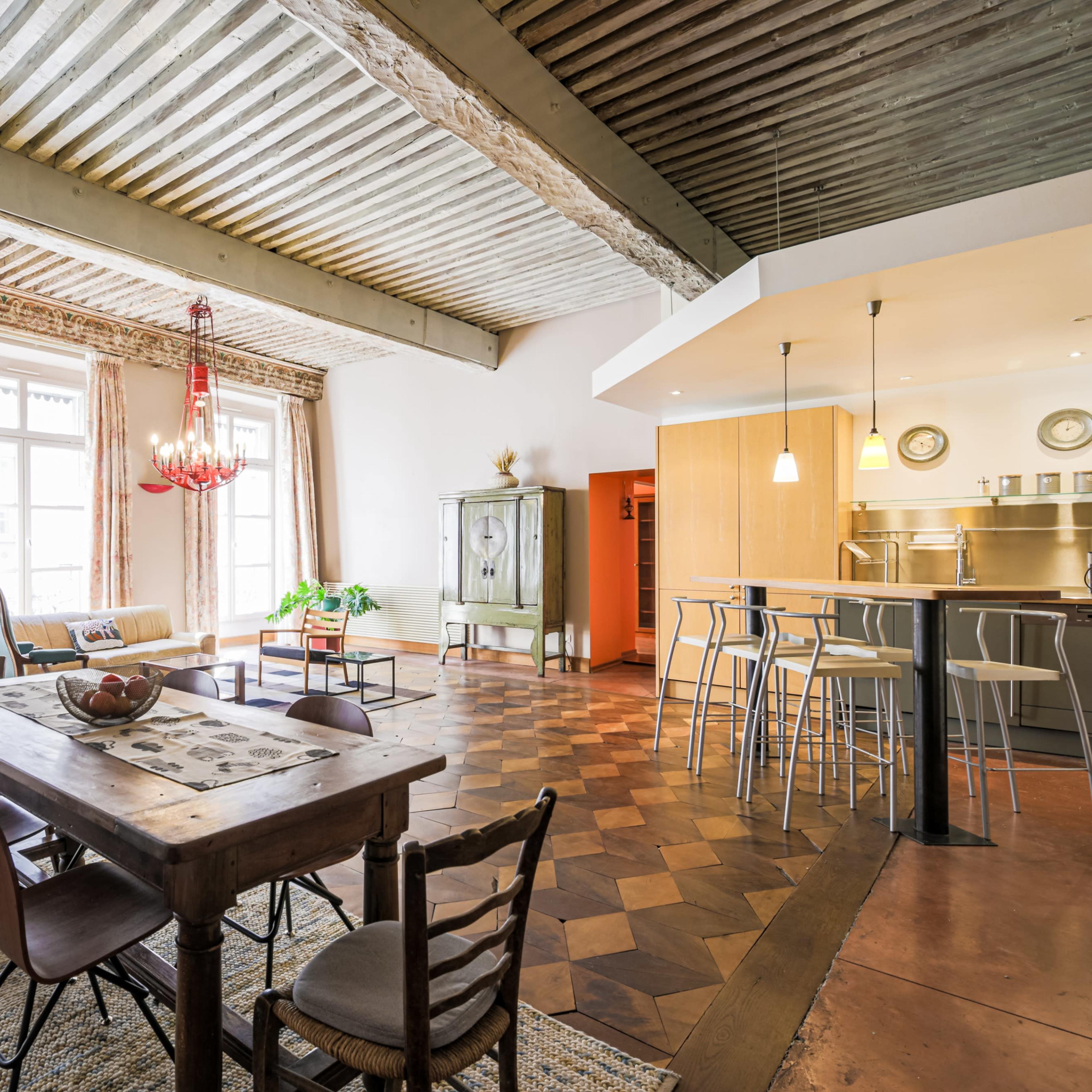 A spacious, well-lit interior featuring a dining table, a lounge area, and a modern kitchen with bar seating.