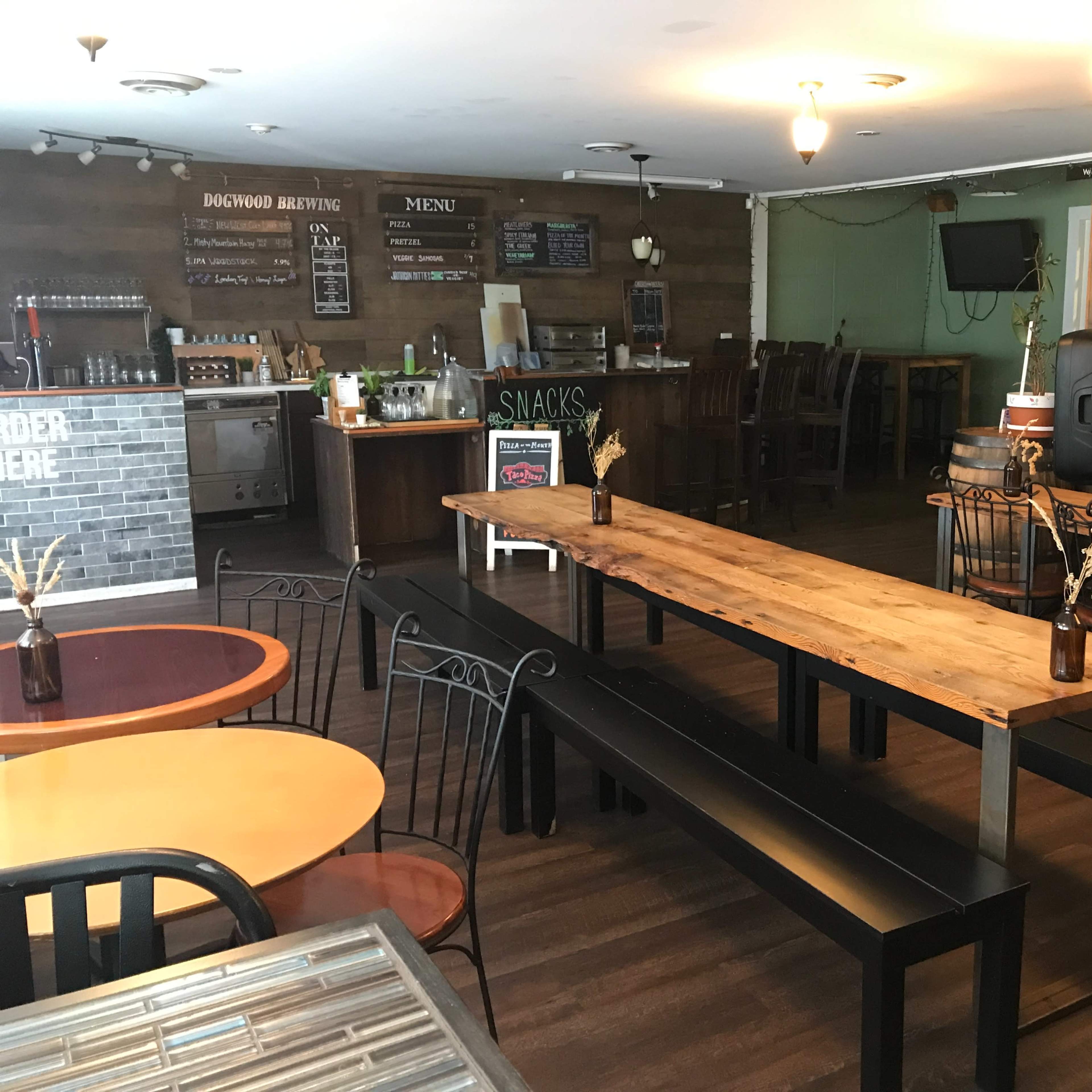 A rustic interior of a brewery with wooden tables, a bar area, and a menu board on the wall.