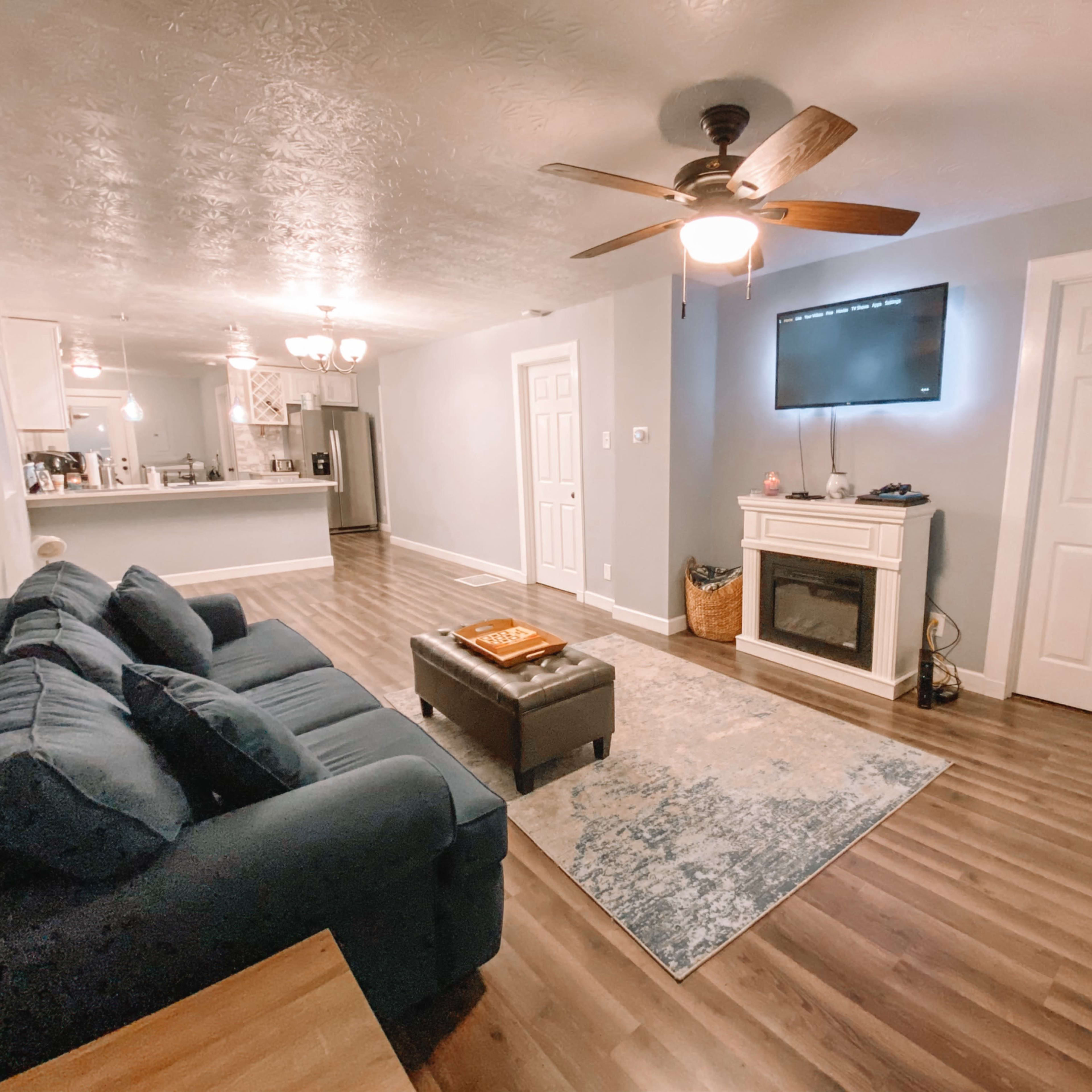 The living room features a blue sofa facing a wall-mounted television above a fireplace, with a coffee table and a patterned rug on the wooden floor.