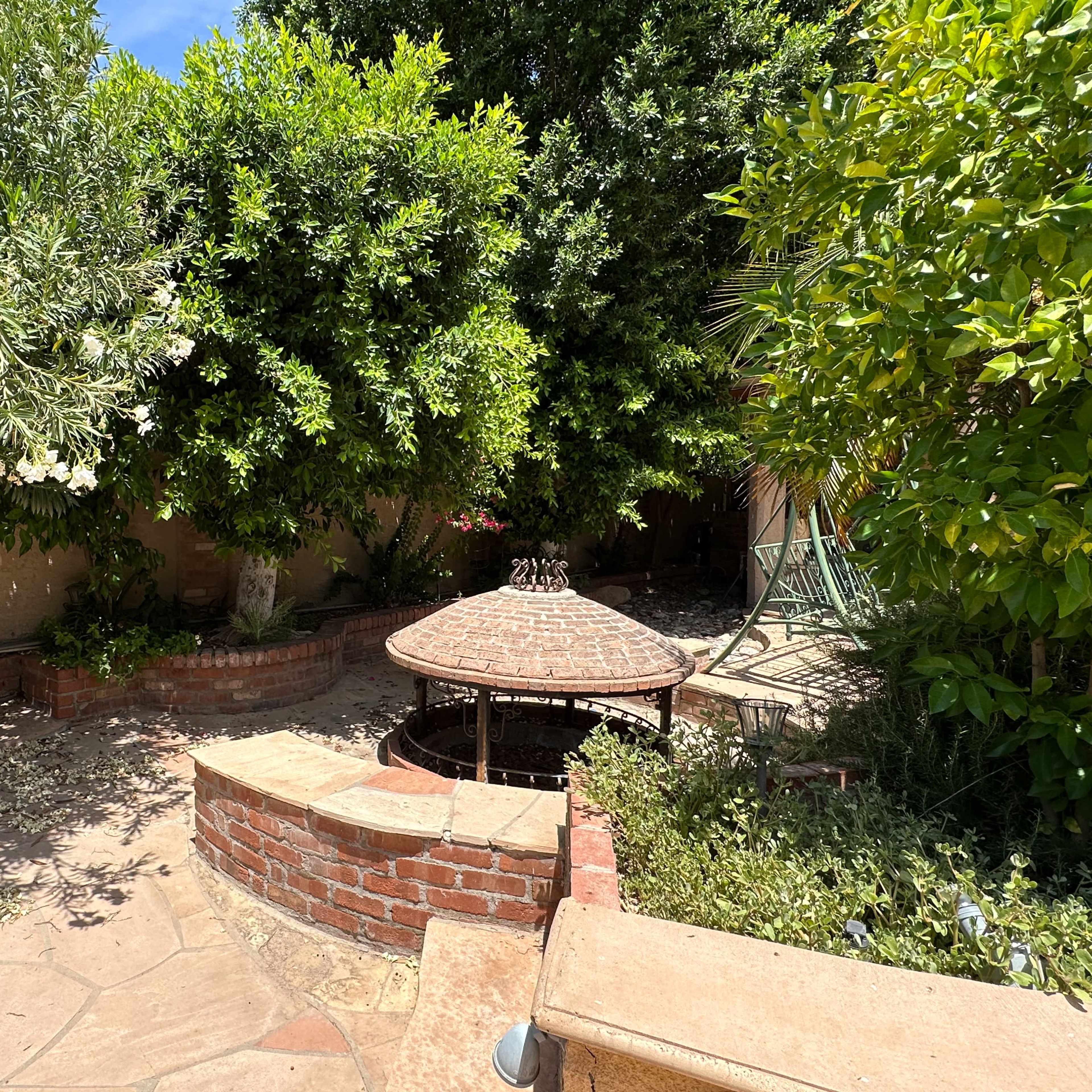 A stone patio surrounded by lush greenery and a gazebo in a garden setting.
