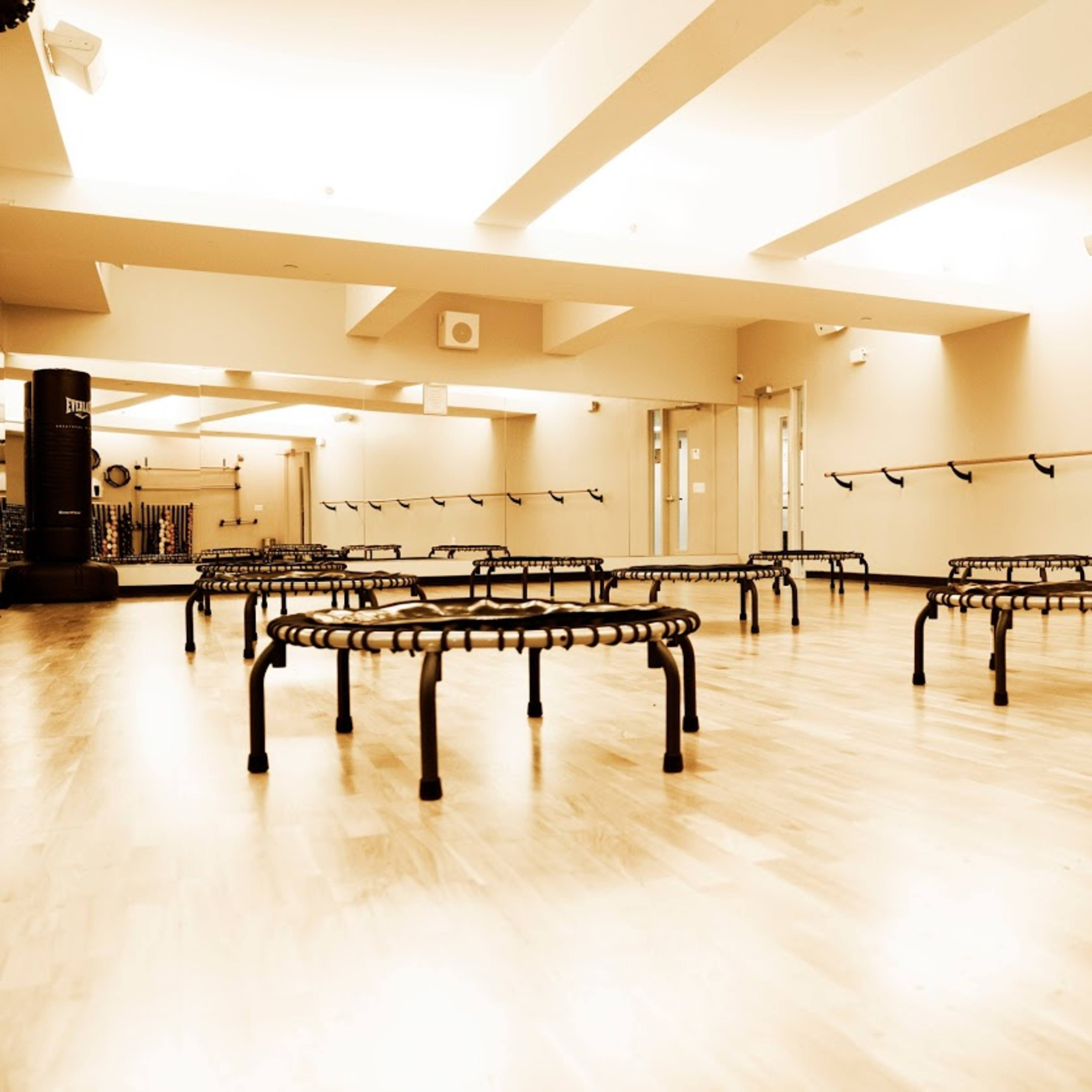 A spacious fitness room with several small, black rebounders arranged on a wooden floor.