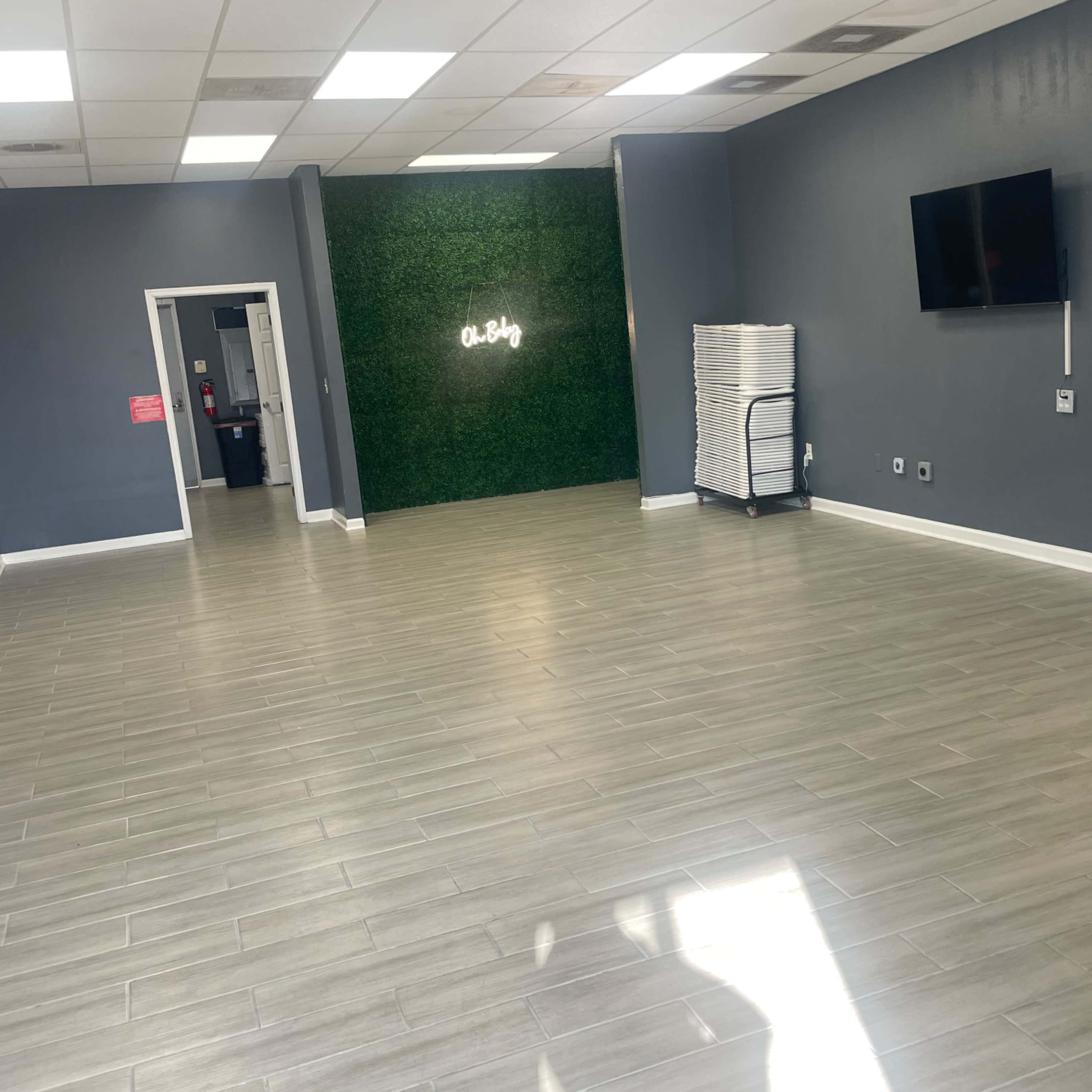 A spacious, empty room with wooden flooring, a green wall feature, and a wall-mounted television.