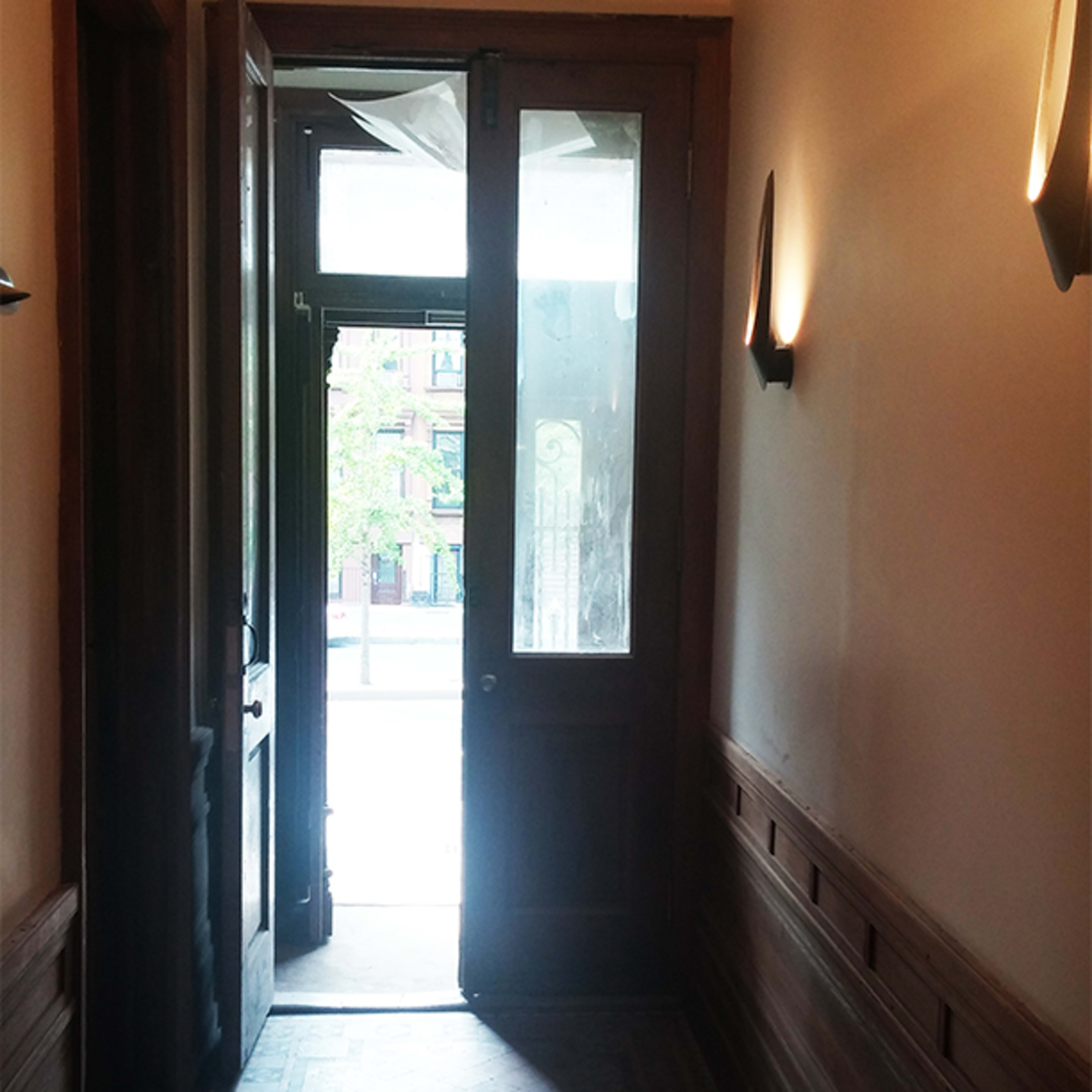 A hallway with wooden paneling and a partially open door leading to a sunny outdoor area.