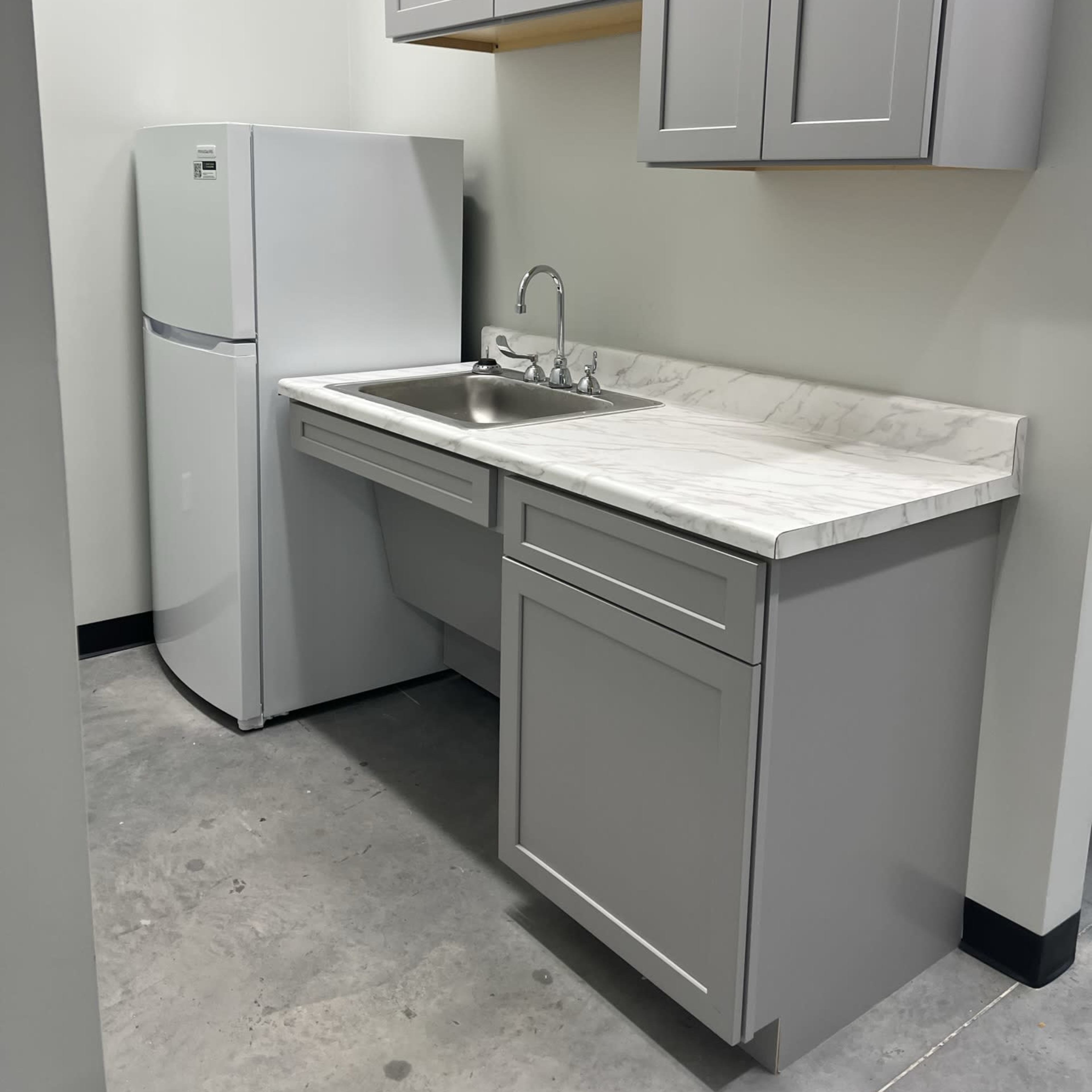 A compact kitchen area with a gray cabinet, sink, and a white refrigerator against a plain wall.