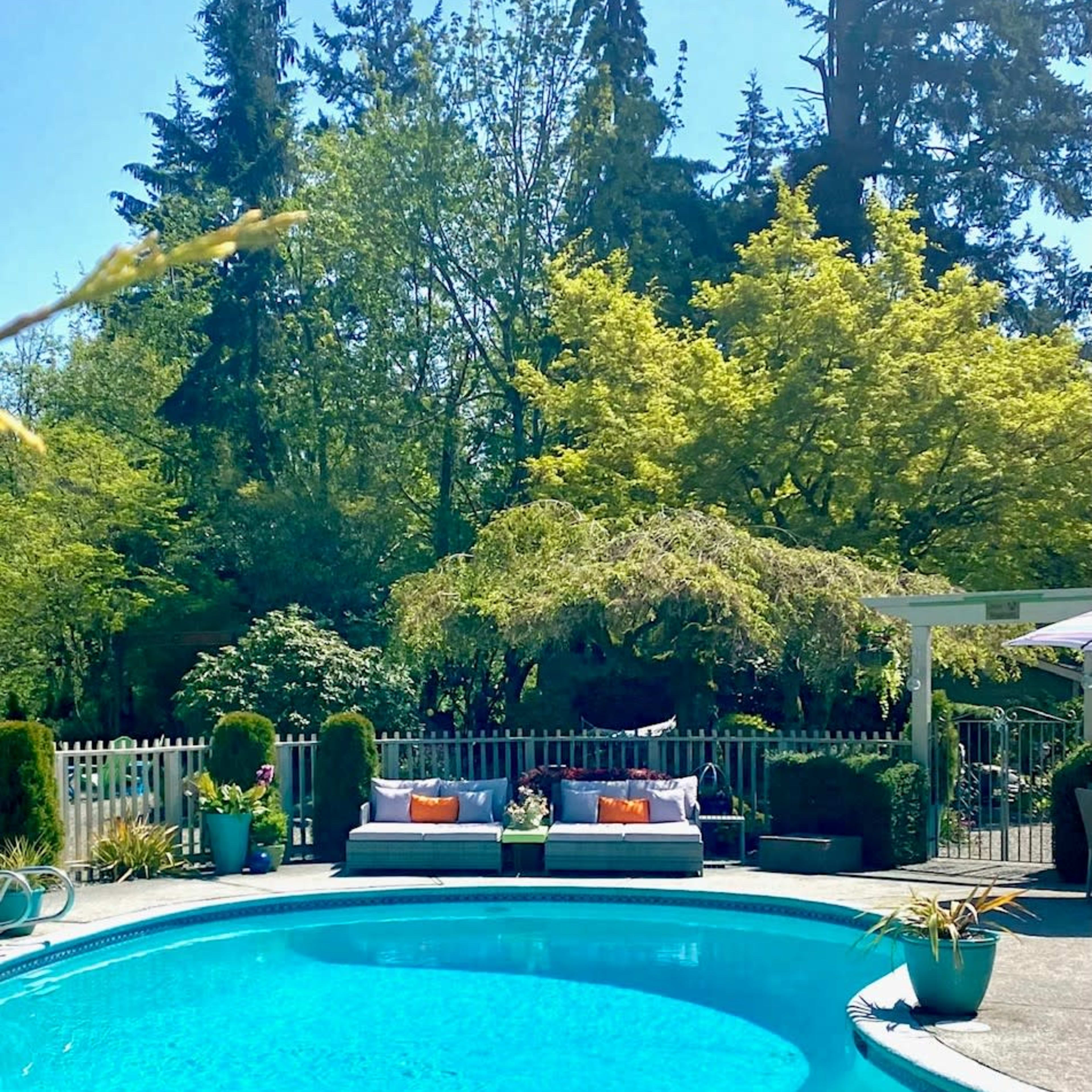 A clear blue pool is surrounded by a landscaped backyard featuring seating areas and lush greenery.