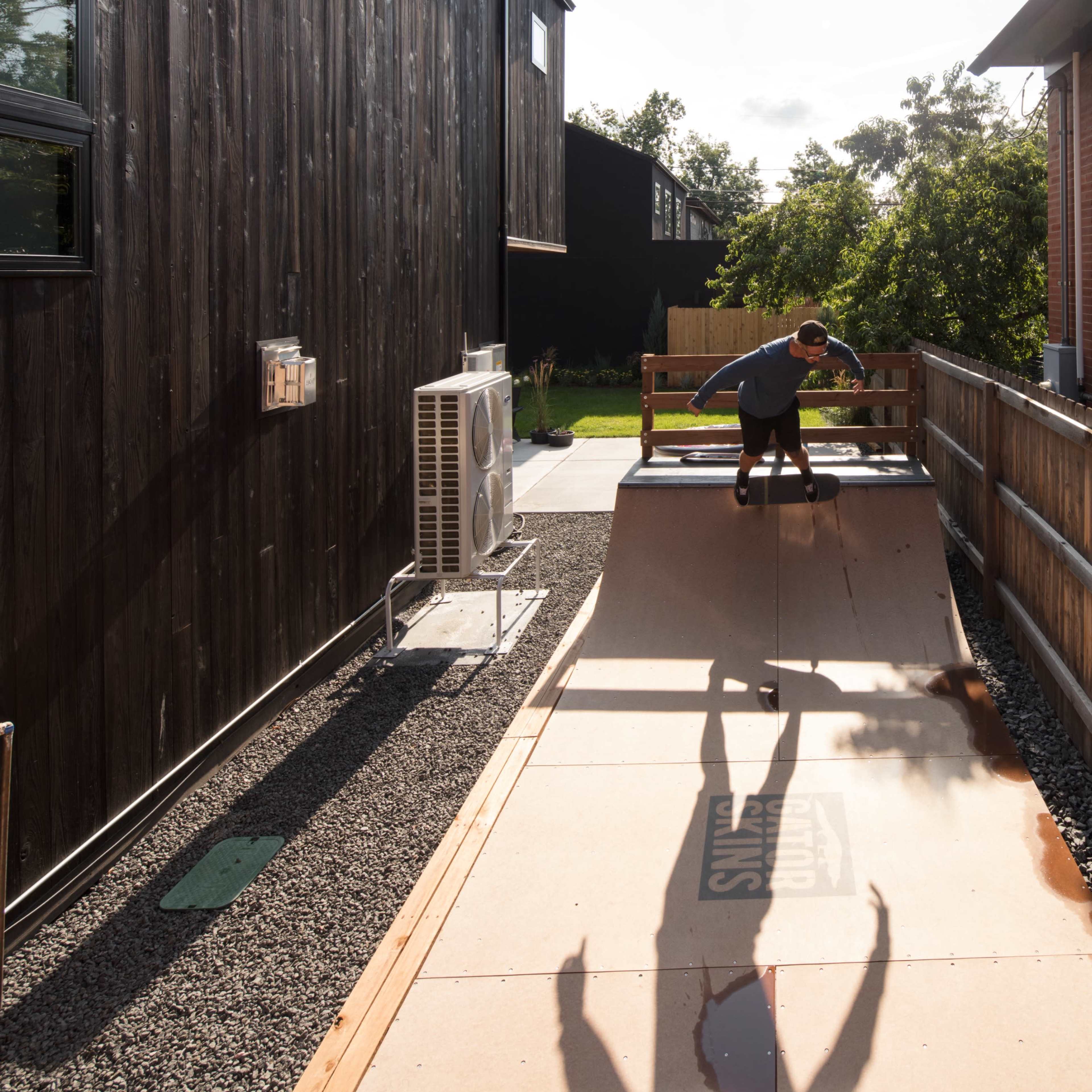 A person performs a skateboarding trick on a wooden ramp located between two modern buildings.