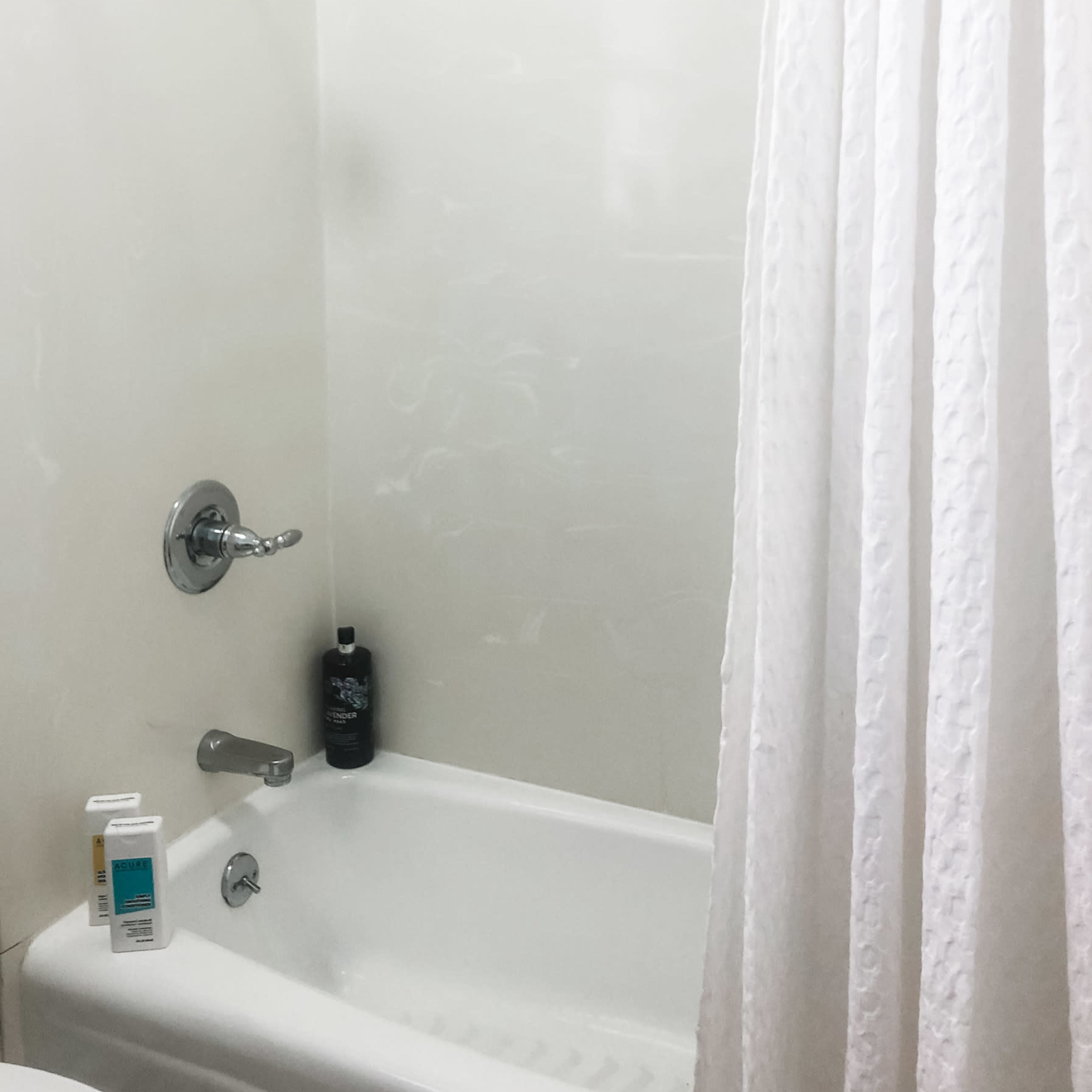A clean bathtub with a showerhead, a shower curtain, and personal care products on the side.