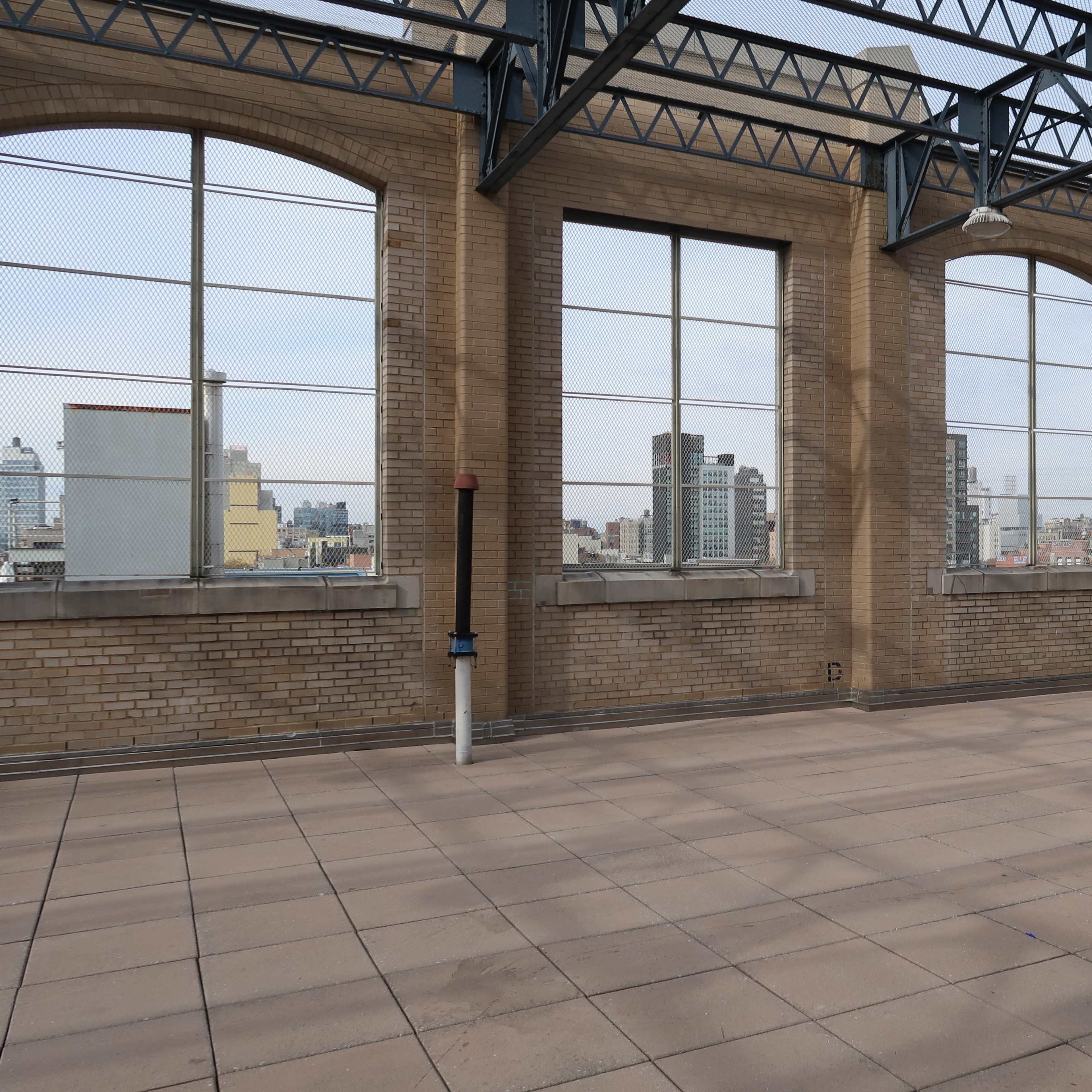 An empty industrial space with large windows and concrete flooring, offering a view of a city skyline in the background.
