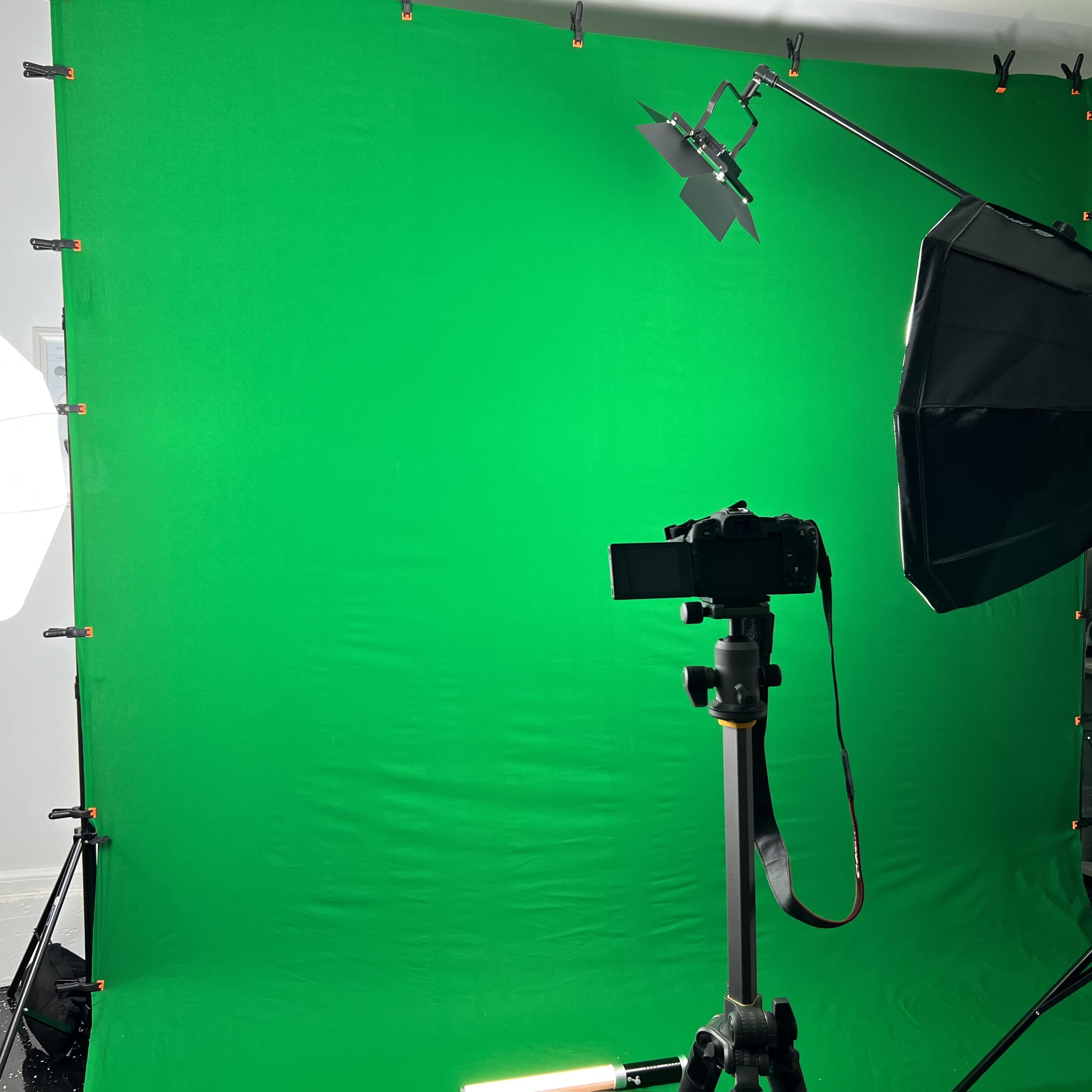 A green screen setup with a camera mounted on a tripod and lighting equipment positioned nearby.