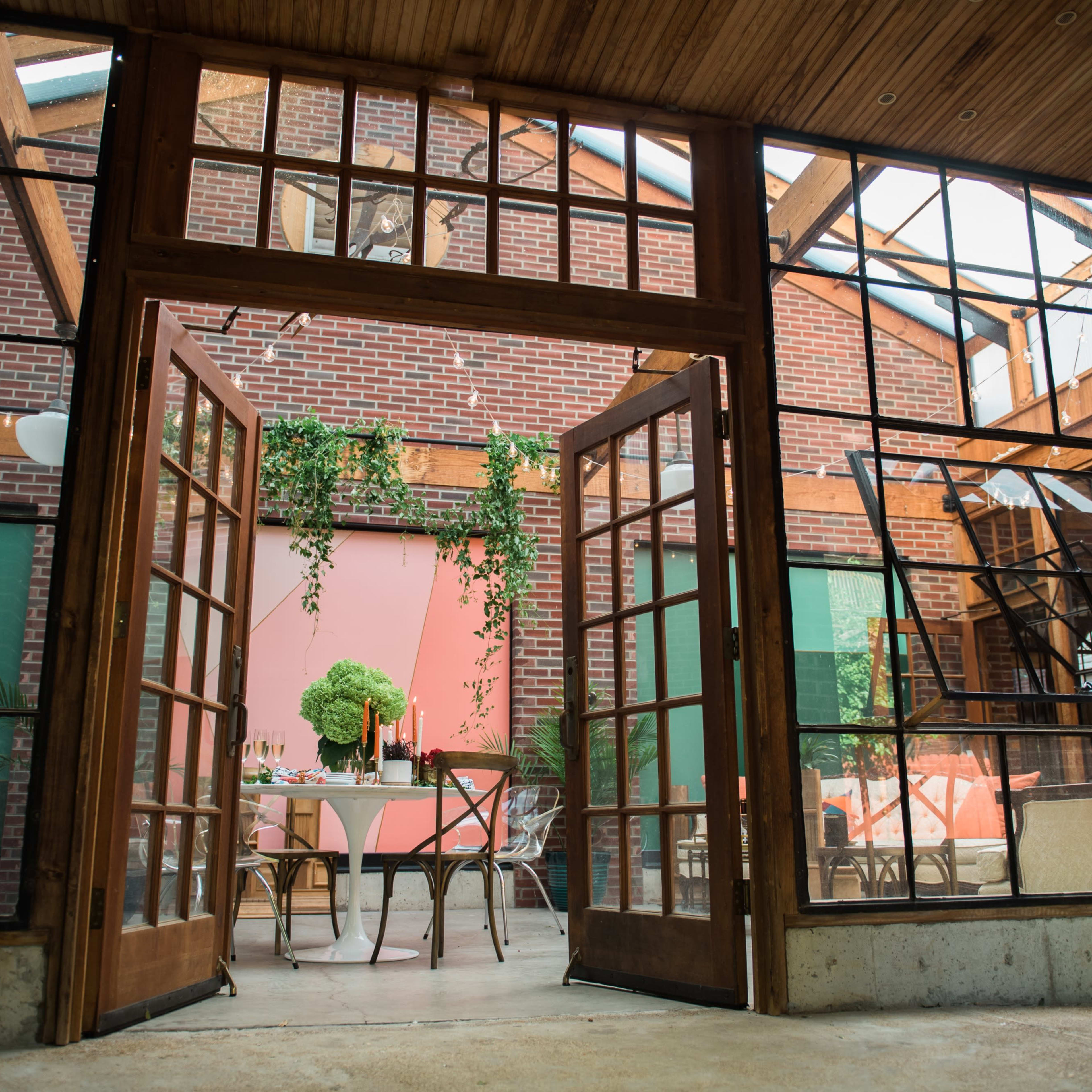 A spacious interior with large glass doors opens to a bright and colorful dining area featuring wooden furniture and greenery.