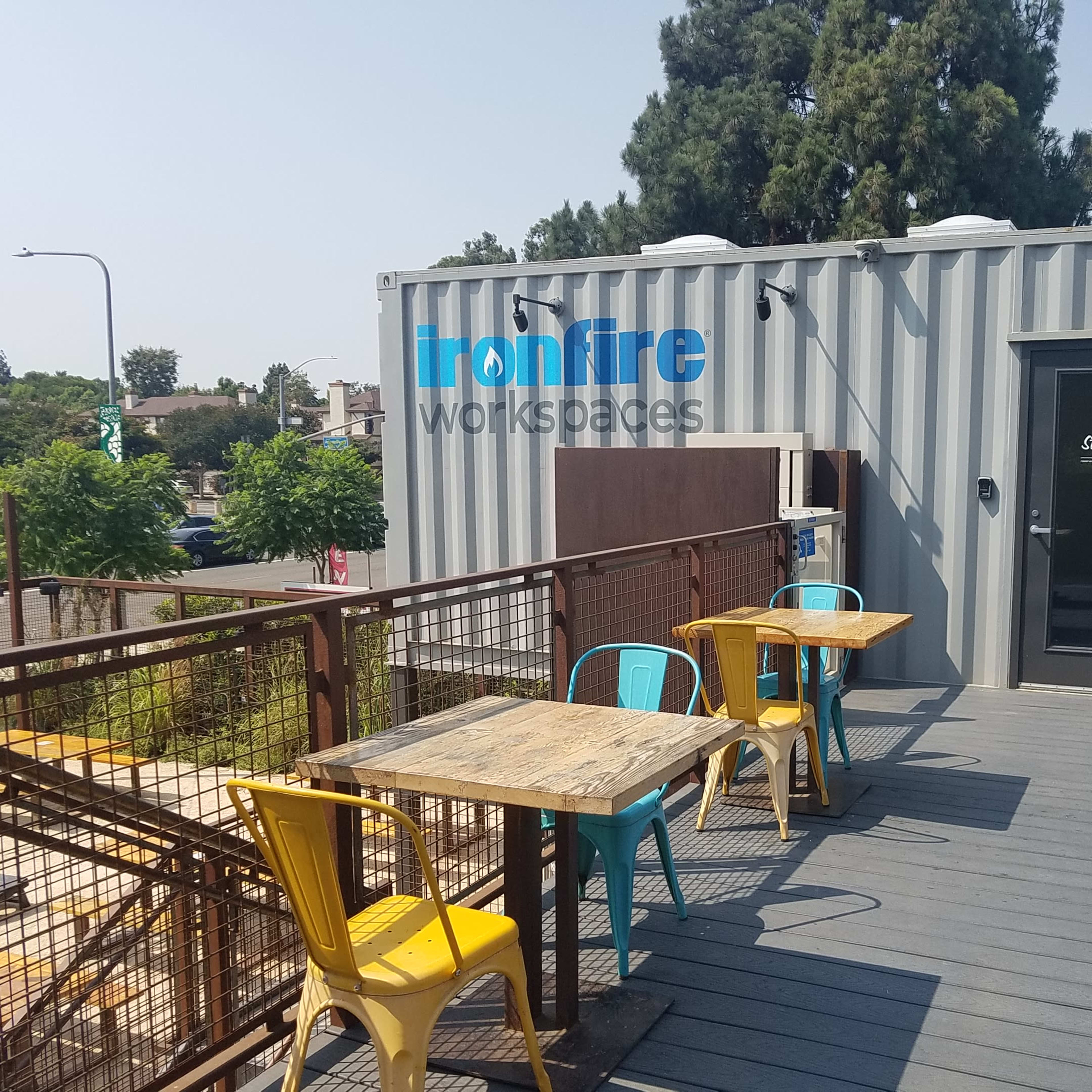 A rooftop area features two blue and yellow chairs with wooden tables beside a shipping container labeled "Ironfire Workspaces."