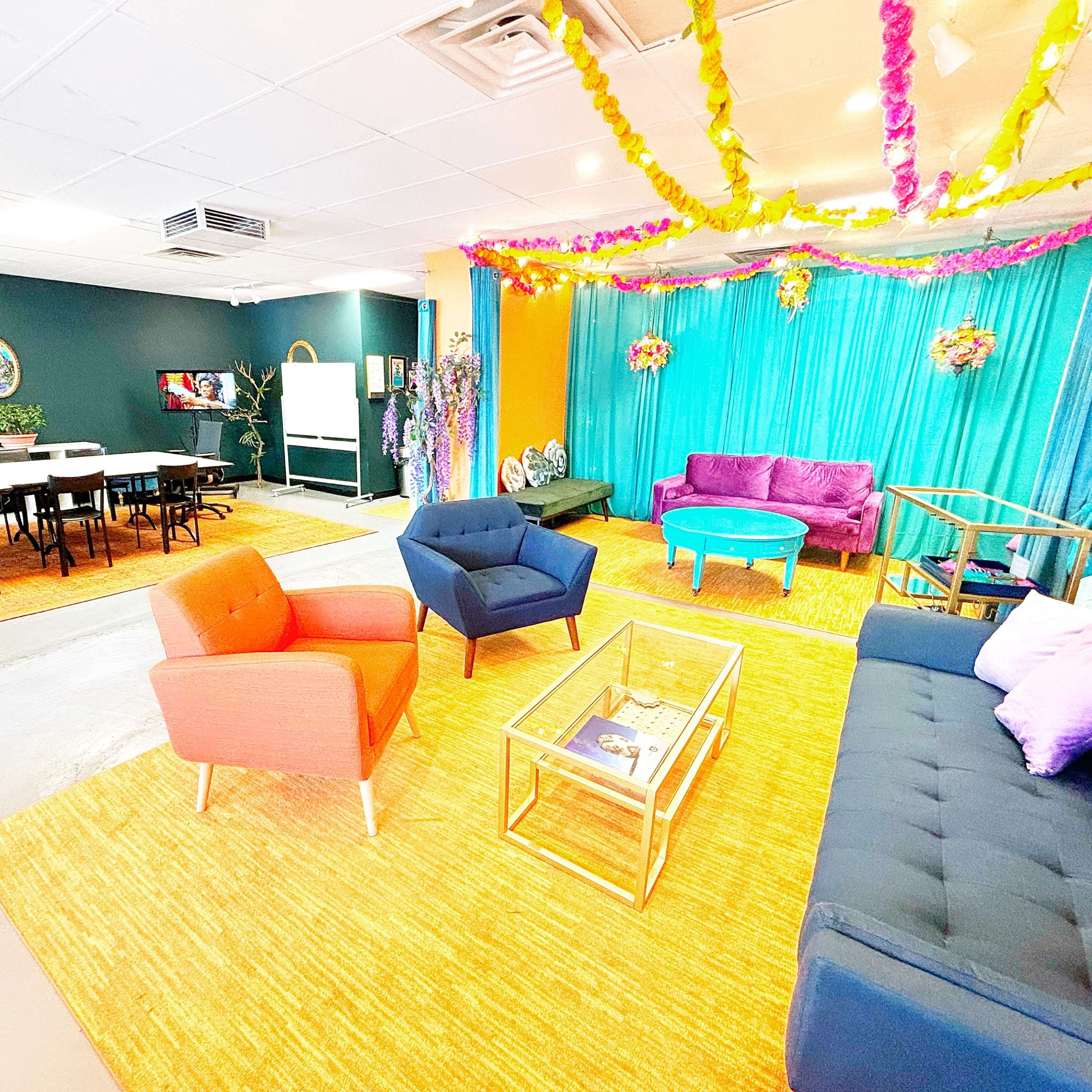 A vibrant room with colorful seating areas, a greenish-blue backdrop, and decorative elements, alongside a dining space with tables and chairs.