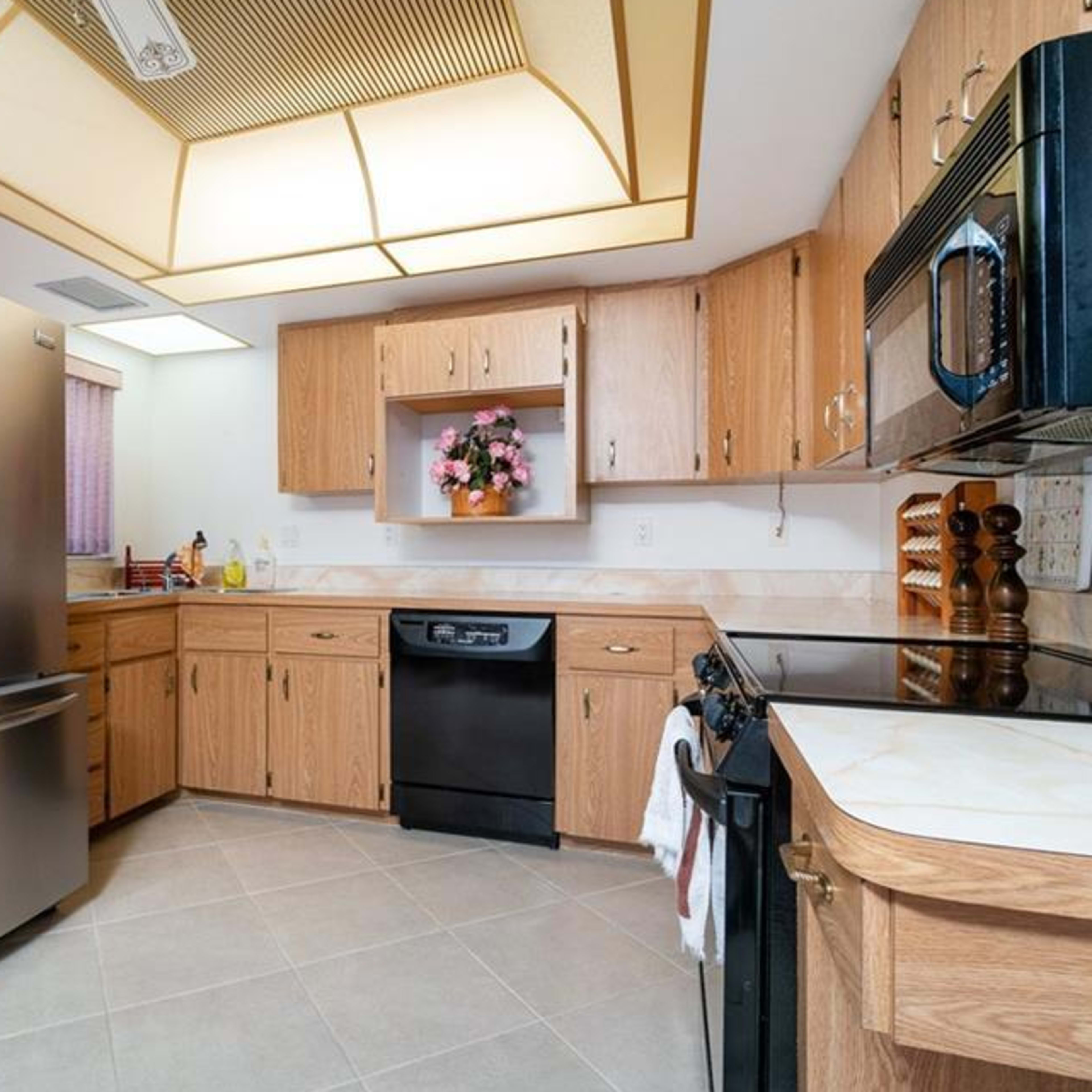 A kitchen with light wood cabinetry, a stainless steel refrigerator, a black dishwasher, and an oven with a microwave above it.