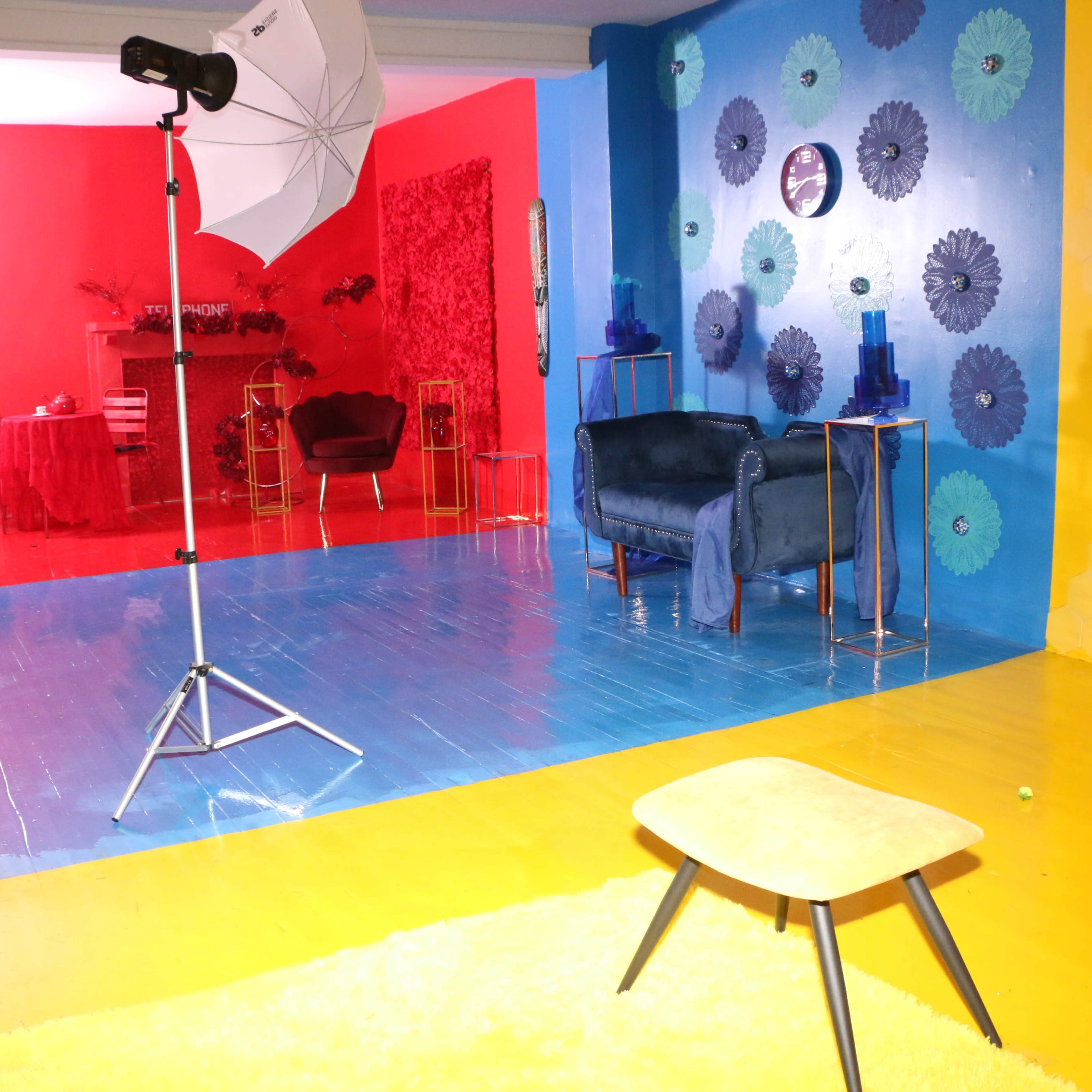 A colorful studio space features a blue and yellow floor, styled furniture, and varying backdrop decorations in red and blue.