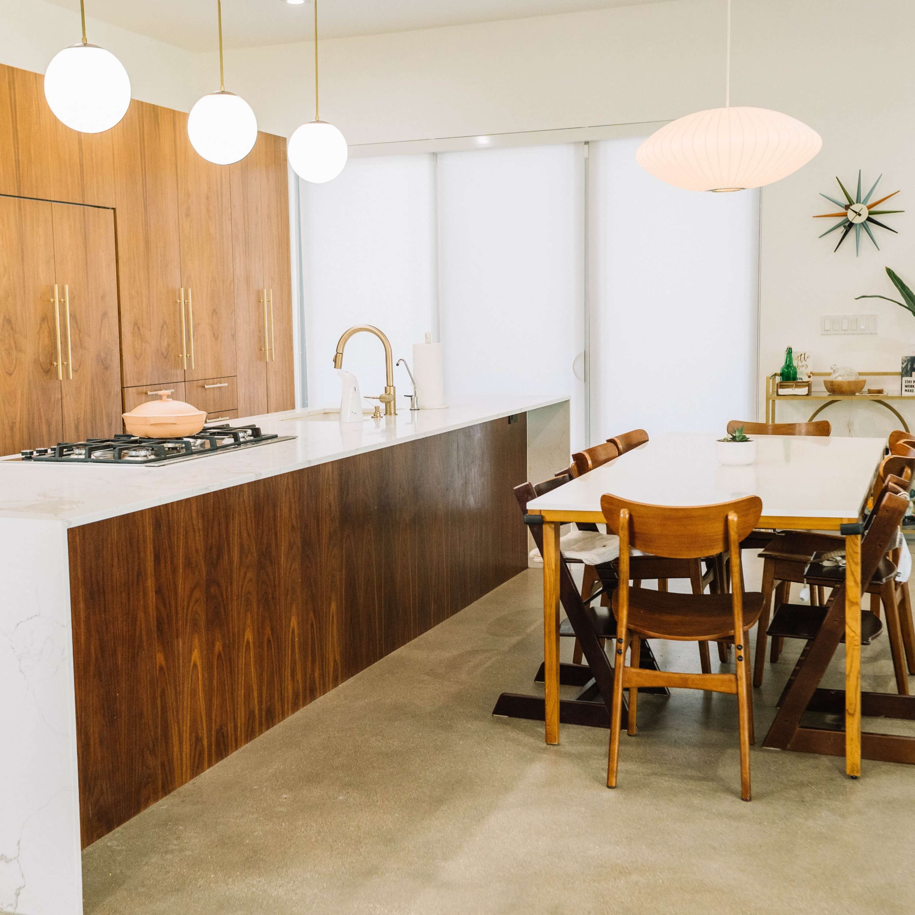 A modern kitchen with wooden cabinetry, a marble countertop, and a dining table surrounded by wooden chairs.