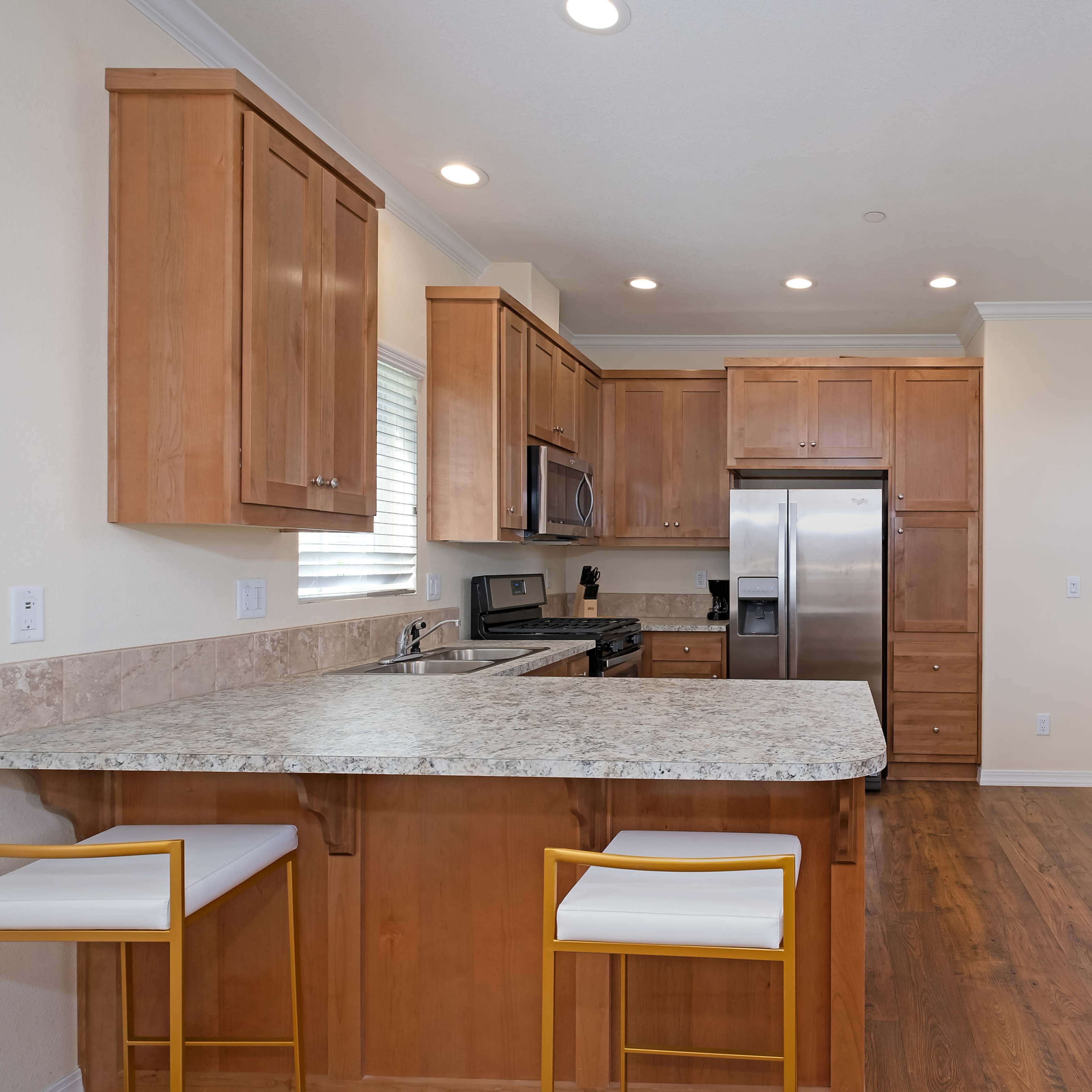 A modern kitchen with wooden cabinetry, granite countertops, stainless steel appliances, and a small dining area with a table and chairs.