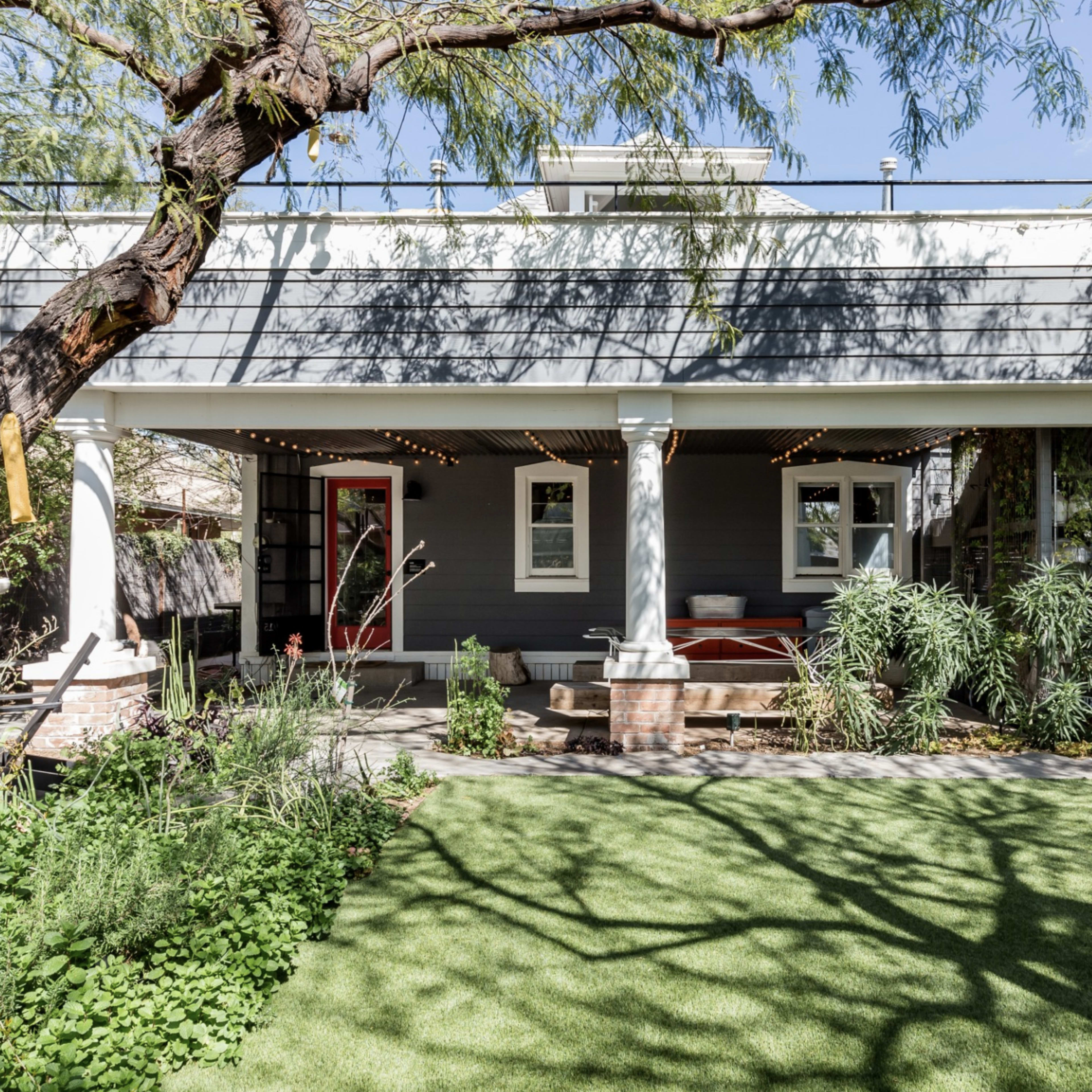 A two-story house with a covered porch, surrounded by greenery and a well-maintained lawn, features columns and decorative string lights.