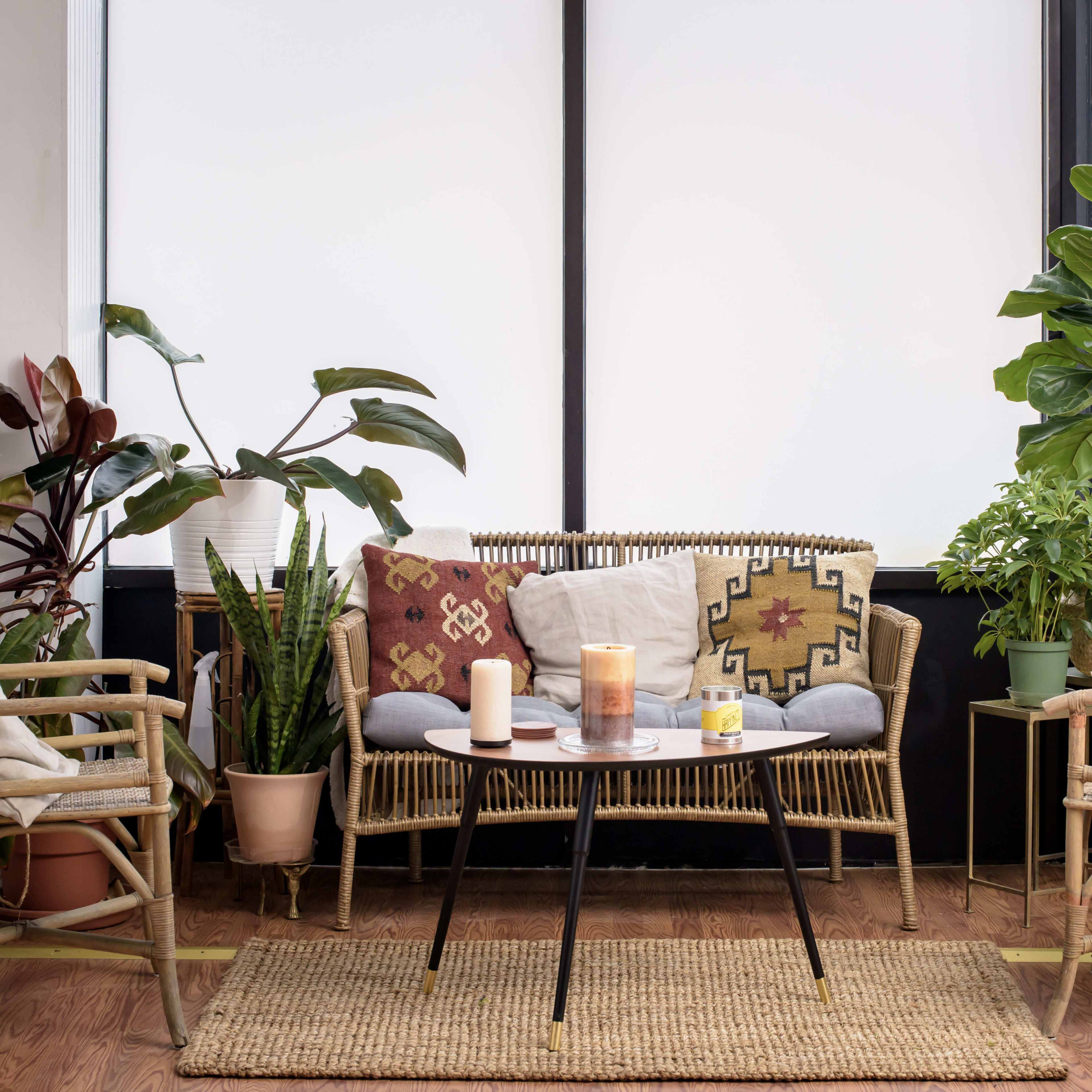 A cozy indoor seating area features a wicker sofa and two matching chairs surrounded by various potted plants and a small table with candles.