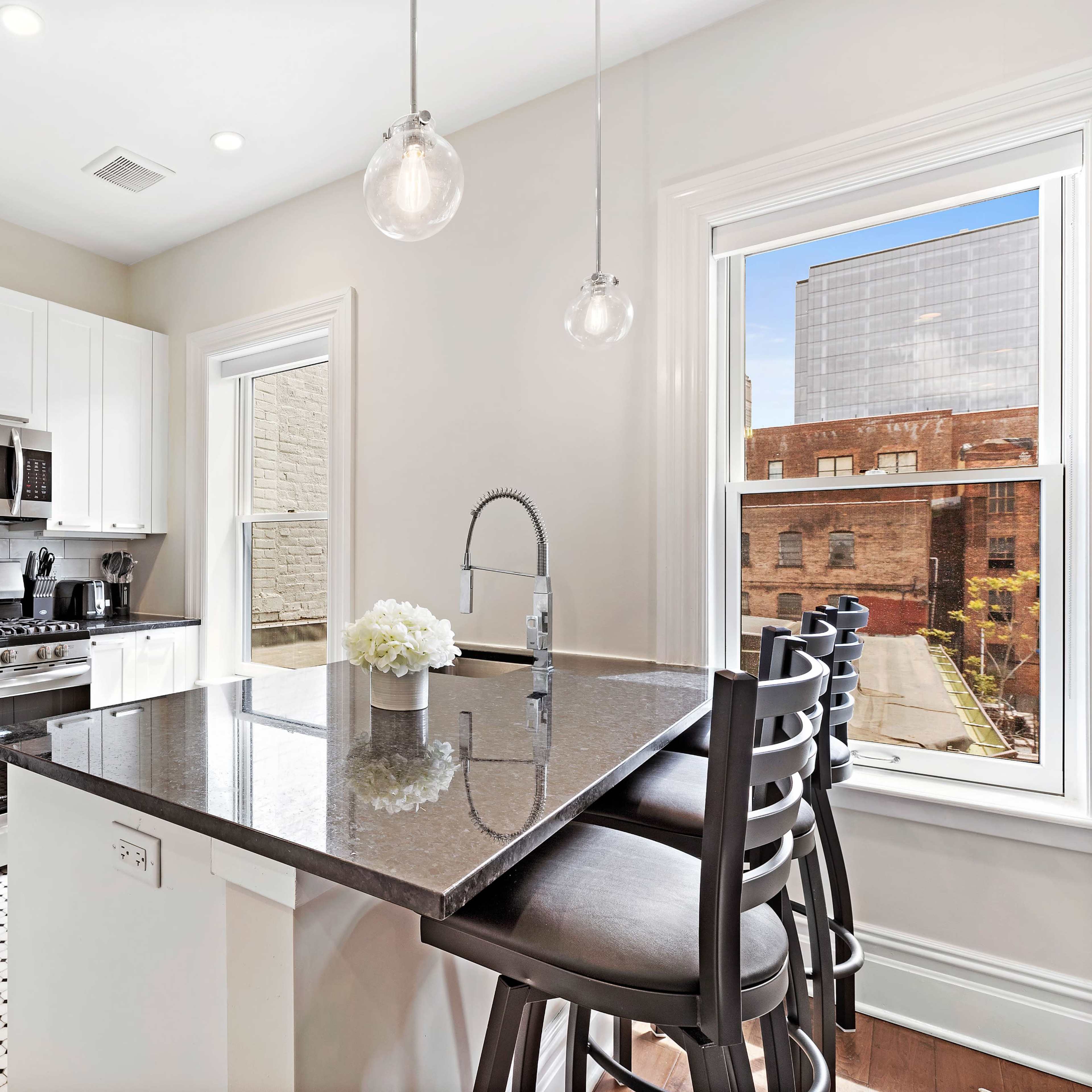 A modern kitchen features stainless steel appliances, white cabinetry, and a dark granite island with seating.