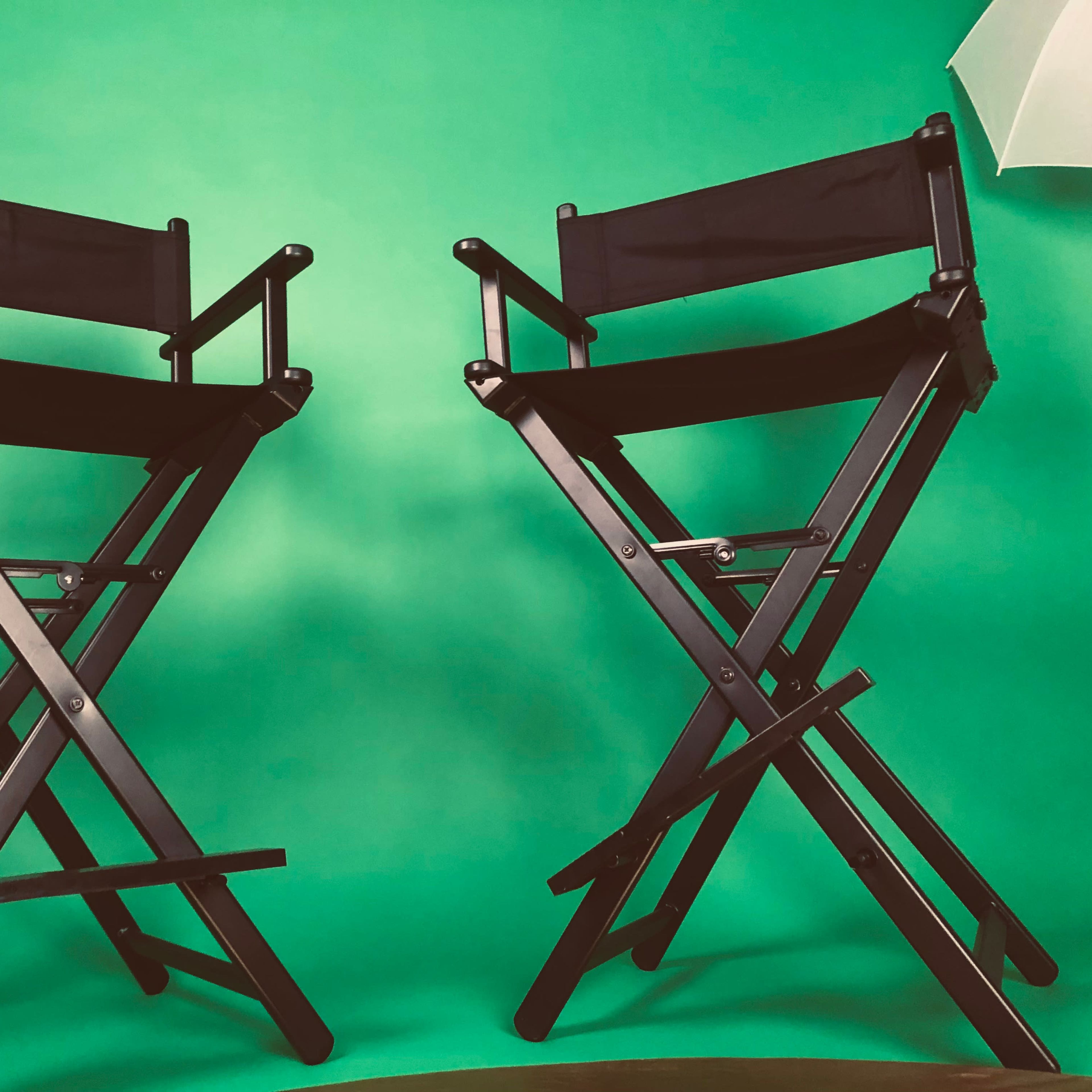 Two black folding director's chairs are positioned in front of a green backdrop.