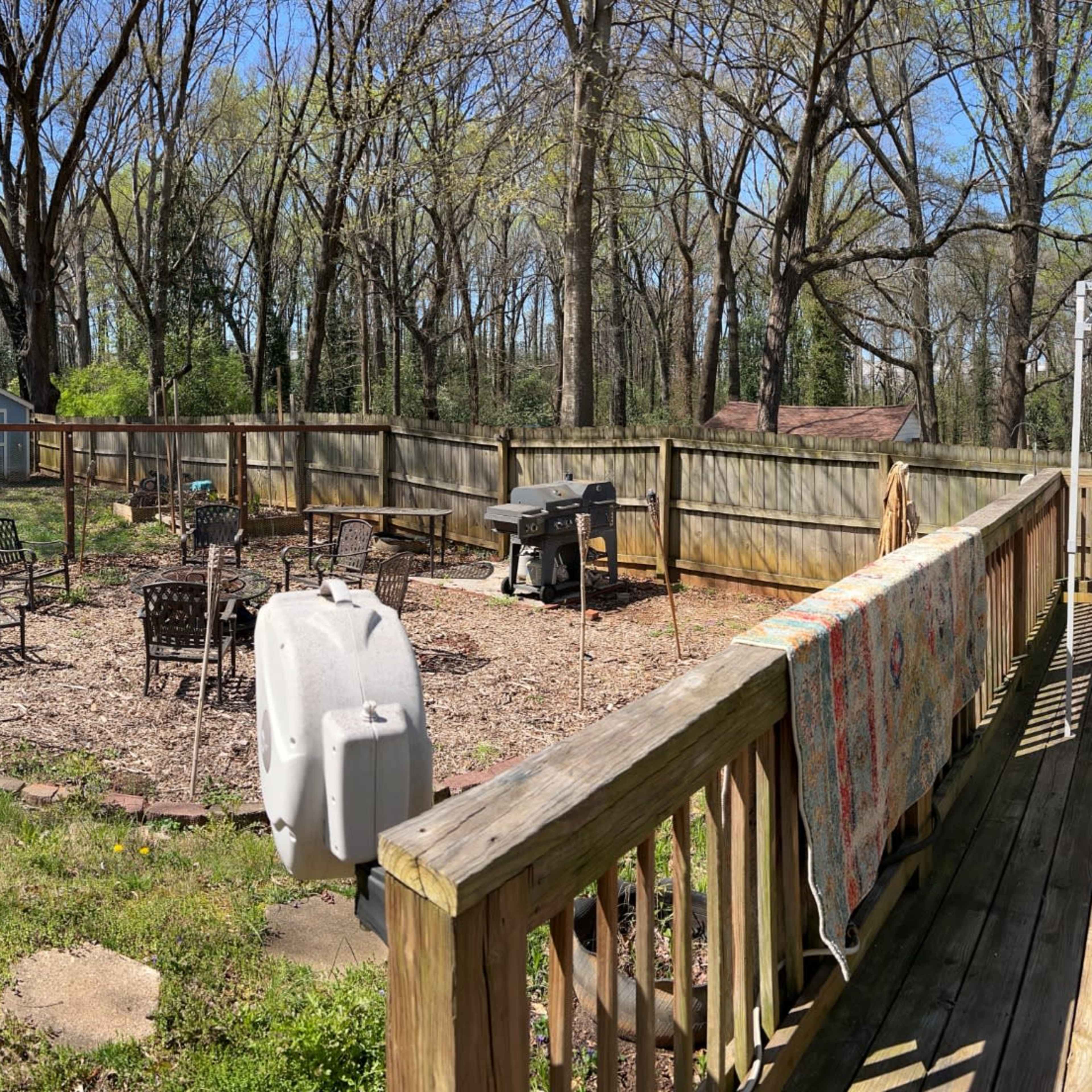 A spacious backyard with a wooden deck, outdoor dining furniture, and a fenced area containing a garden and a small shed.