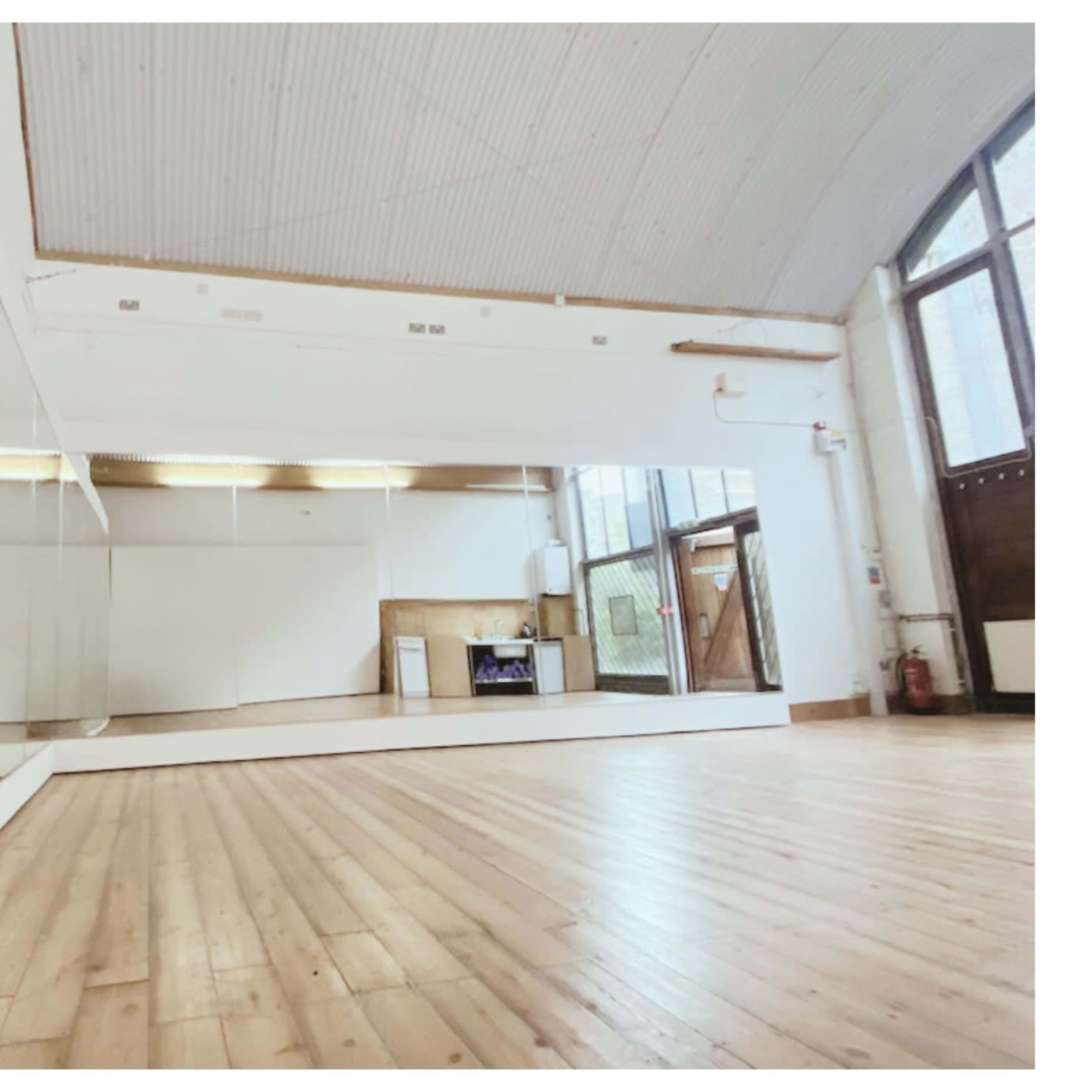A spacious room with wooden flooring, large mirrors on one wall, and a bright, open atmosphere.
