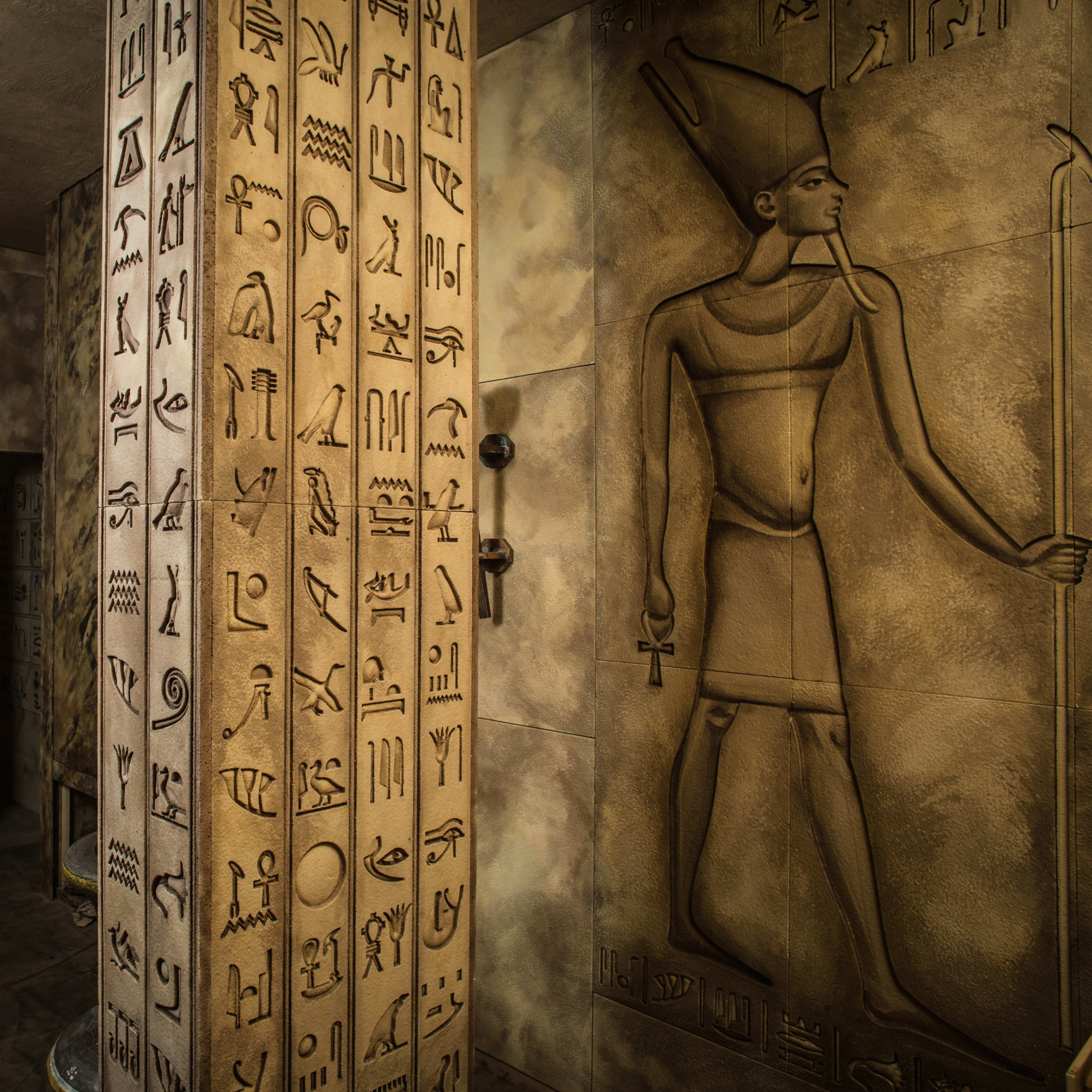 An ancient Egyptian-themed interior with a tall pillar covered in hieroglyphics and a statue of a deity beside a wall carving of a pharaoh.