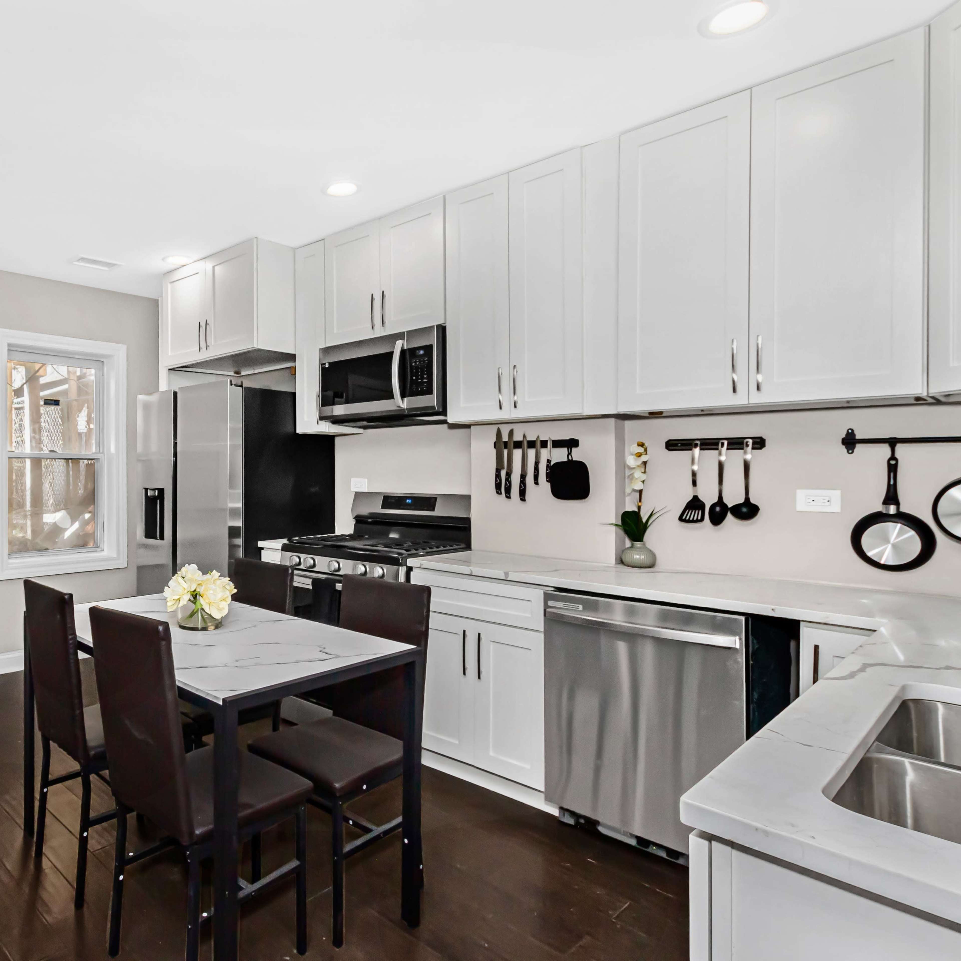 A modern kitchen featuring a small dining table with chairs, stainless steel appliances, and light gray cabinetry.