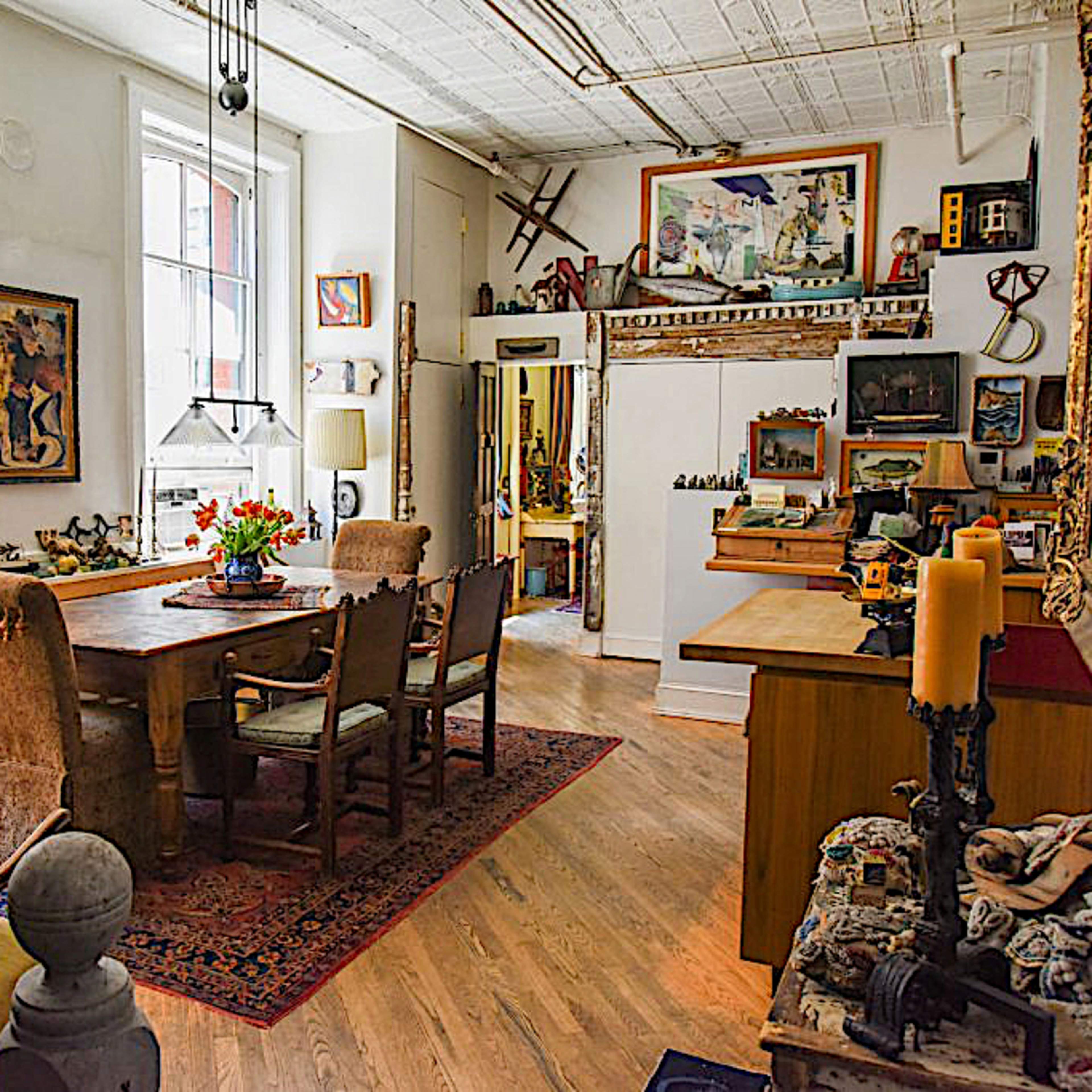A well-furnished room with a dining table, chairs, artwork on the walls, and various decorative items displayed on surfaces.
