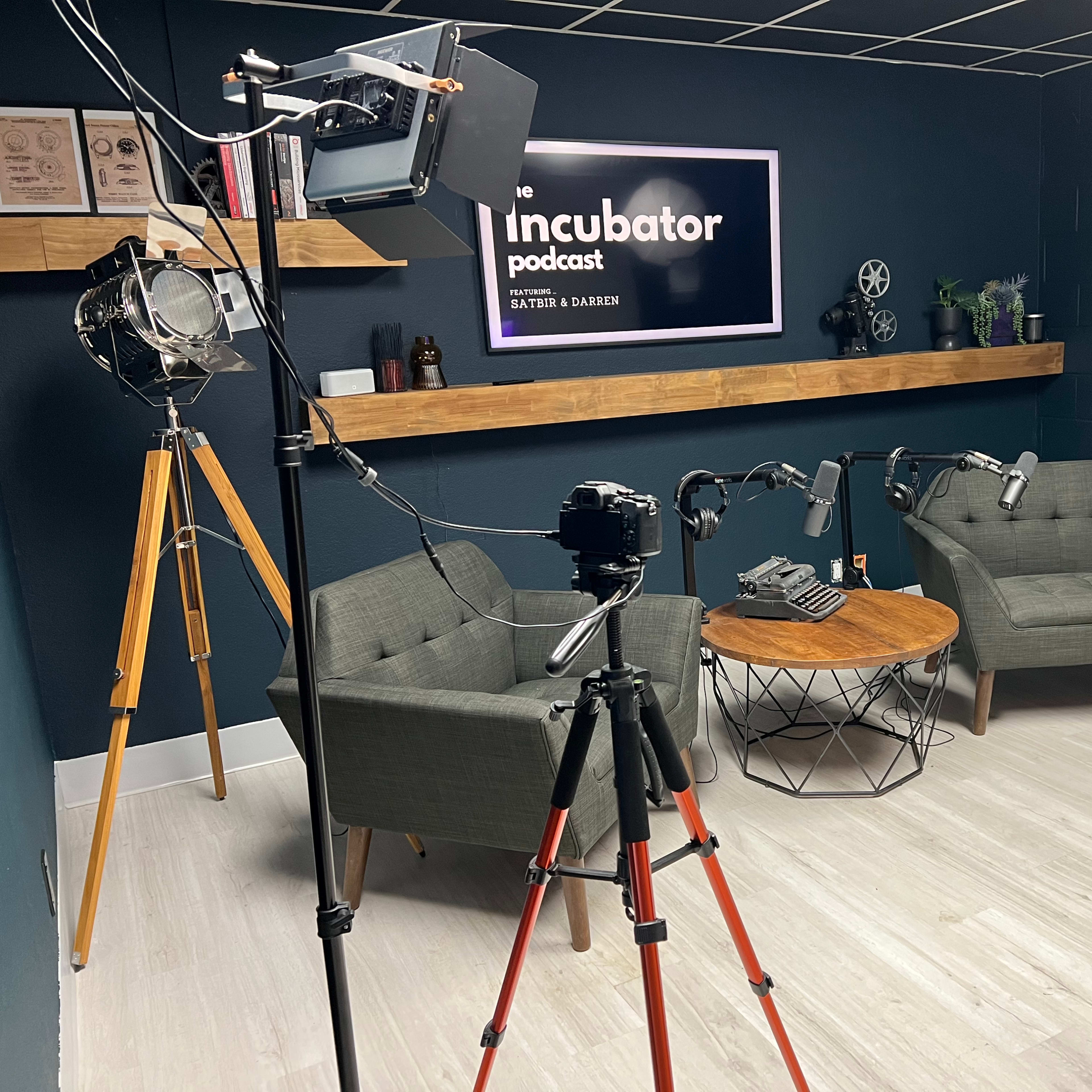 A podcast recording studio featuring two gray armchairs, a round coffee table, and various filming equipment.